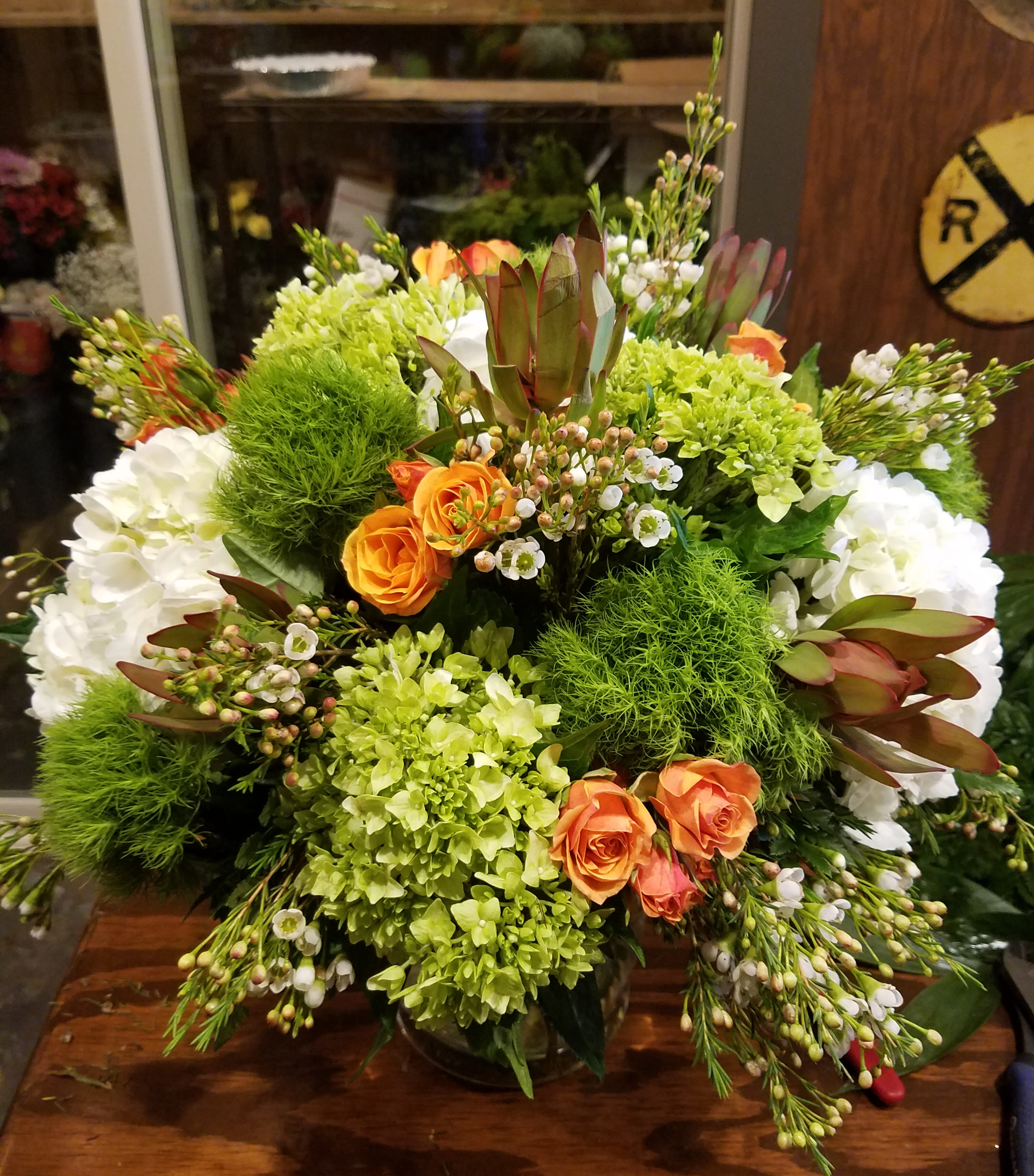 Large bouquet of orange roses, white hydrangeas, and green blooms in a glass vase