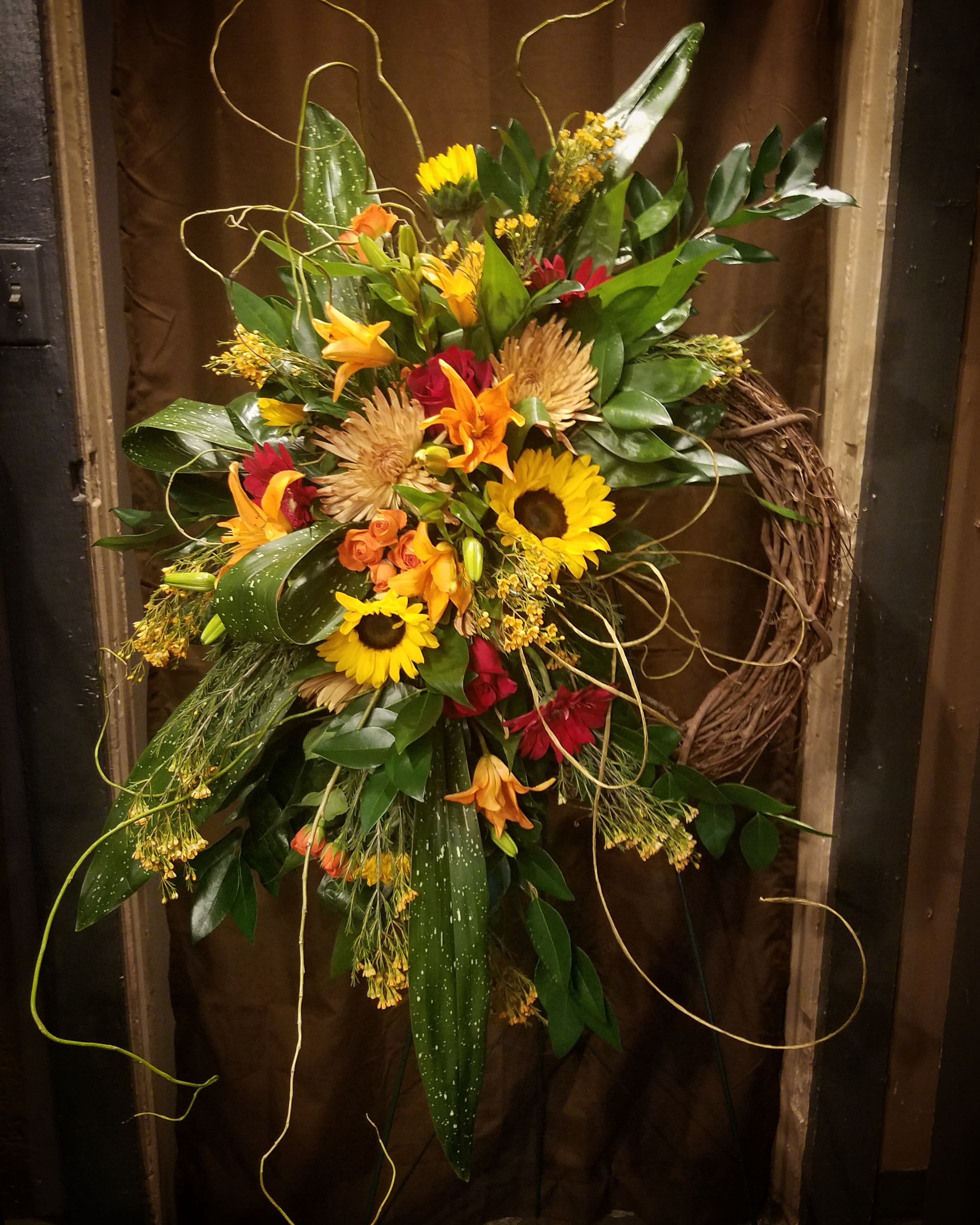 Autumn Tribute wreath - A grapevine wreath showcasing sunflowers and other assorted seasonal fall blooms with a large variety of mixed greenery. 