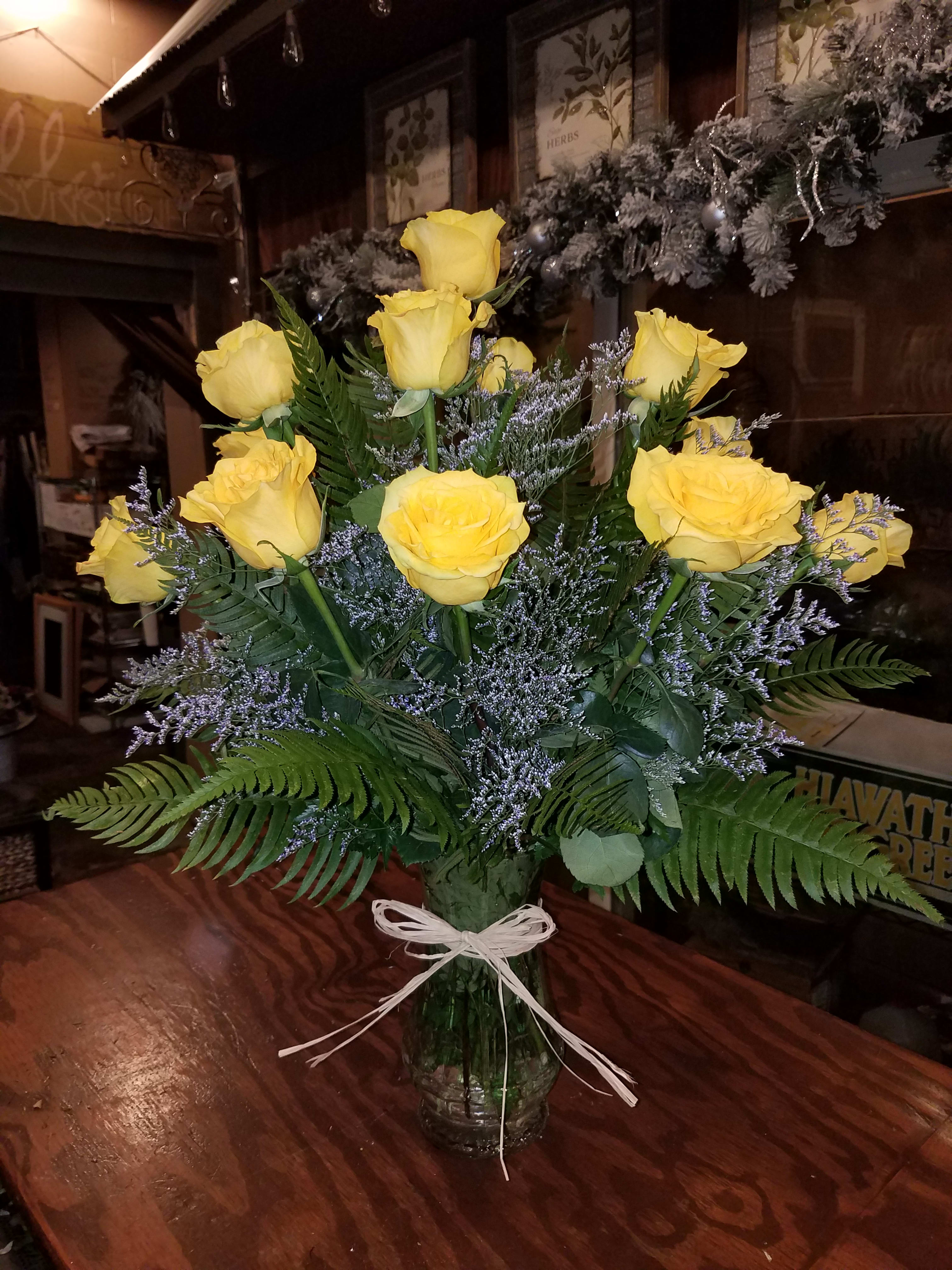Yellow roses arranged in a clear glass vase with a white ribbon