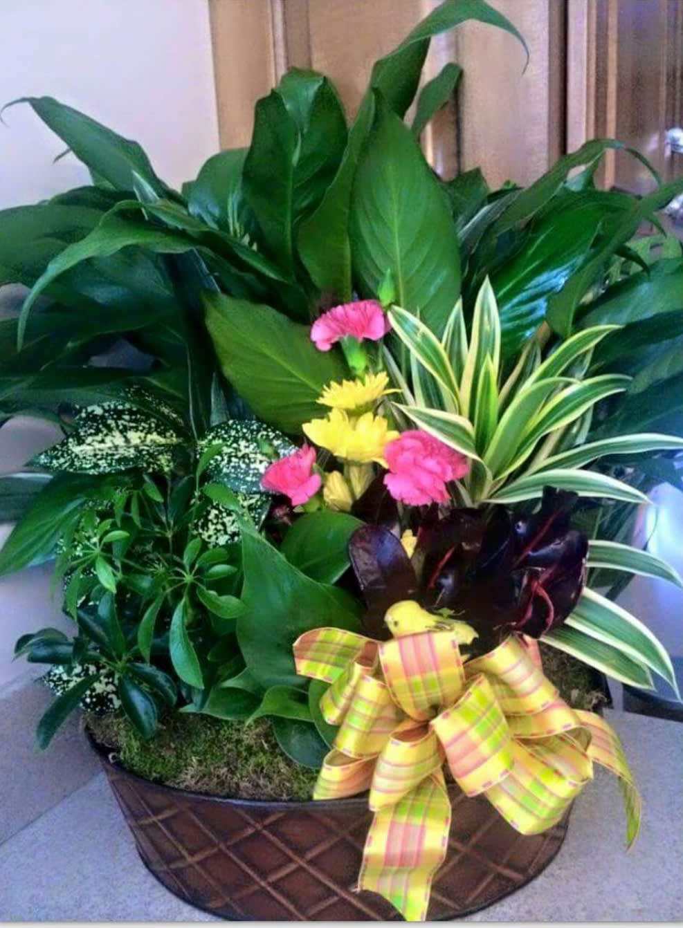 Tropical plant arrangement with pink and yellow flowers in a basket