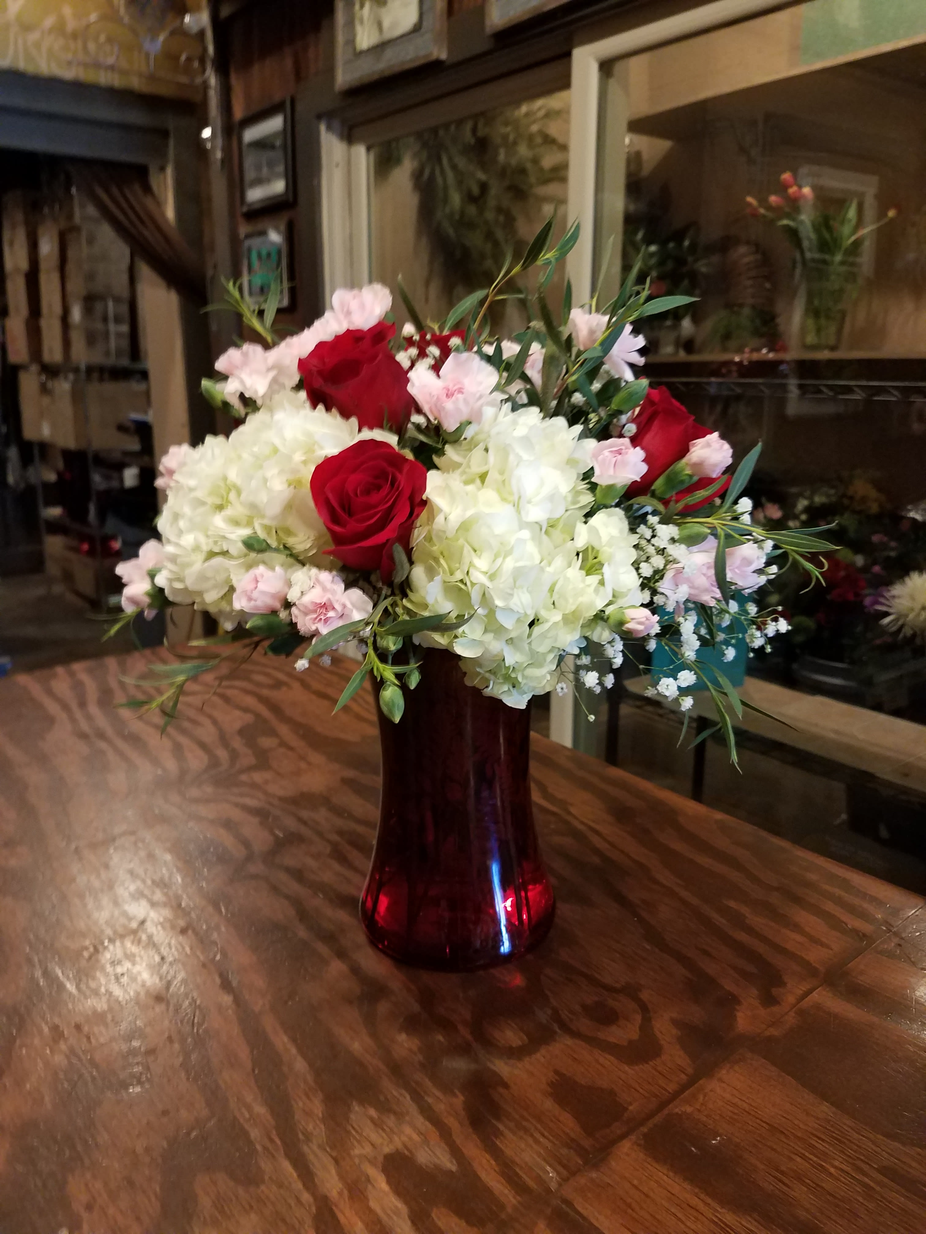 Bouquet of red roses, white hydrangeas, and pink carnations in a red glass vase