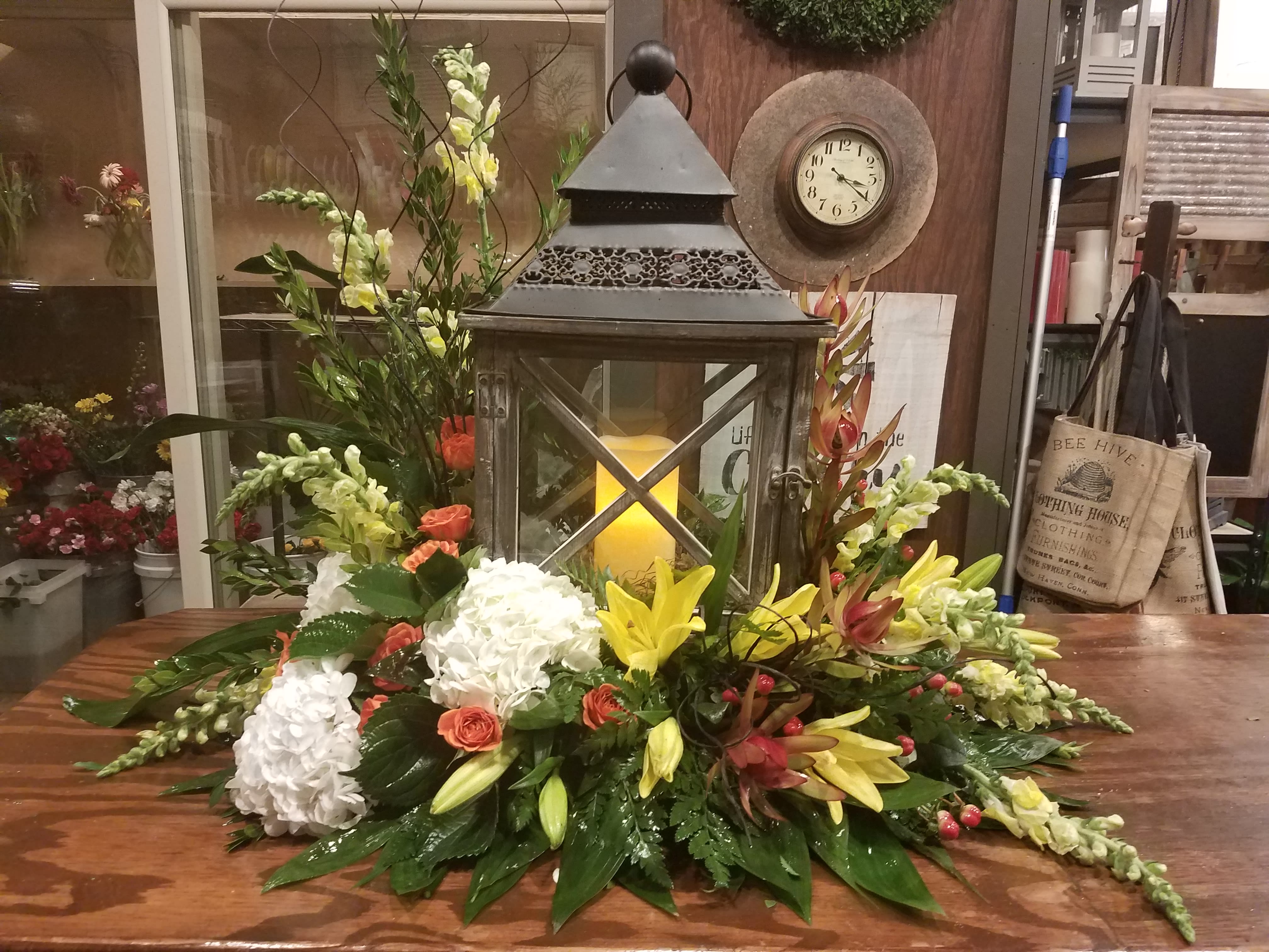 Low floral centerpiece with white hydrangeas, yellow lilies, and coral roses around a lantern.