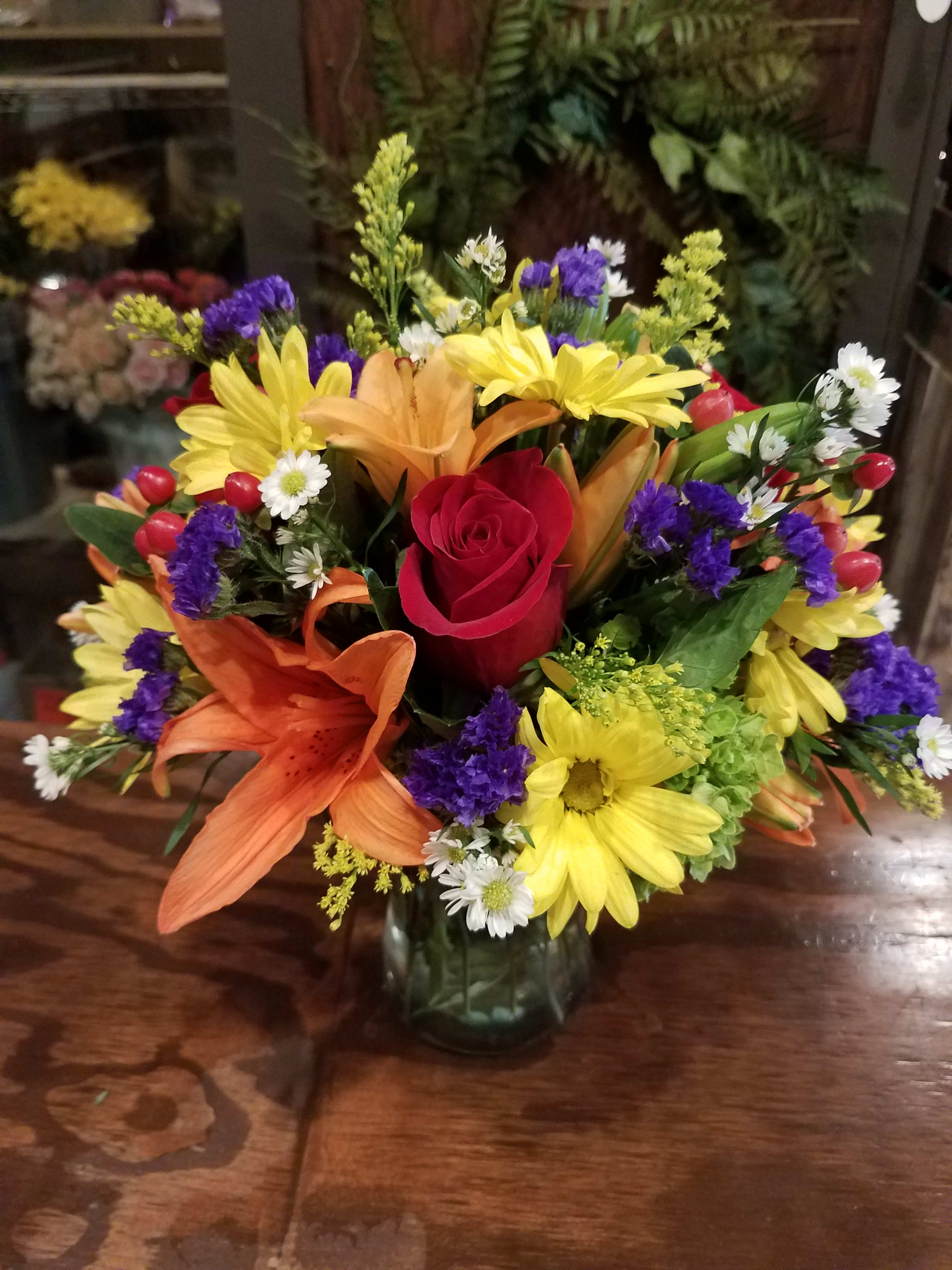 Mixed bouquet with a red rose, lilies, and yellow daisies in a glass vase