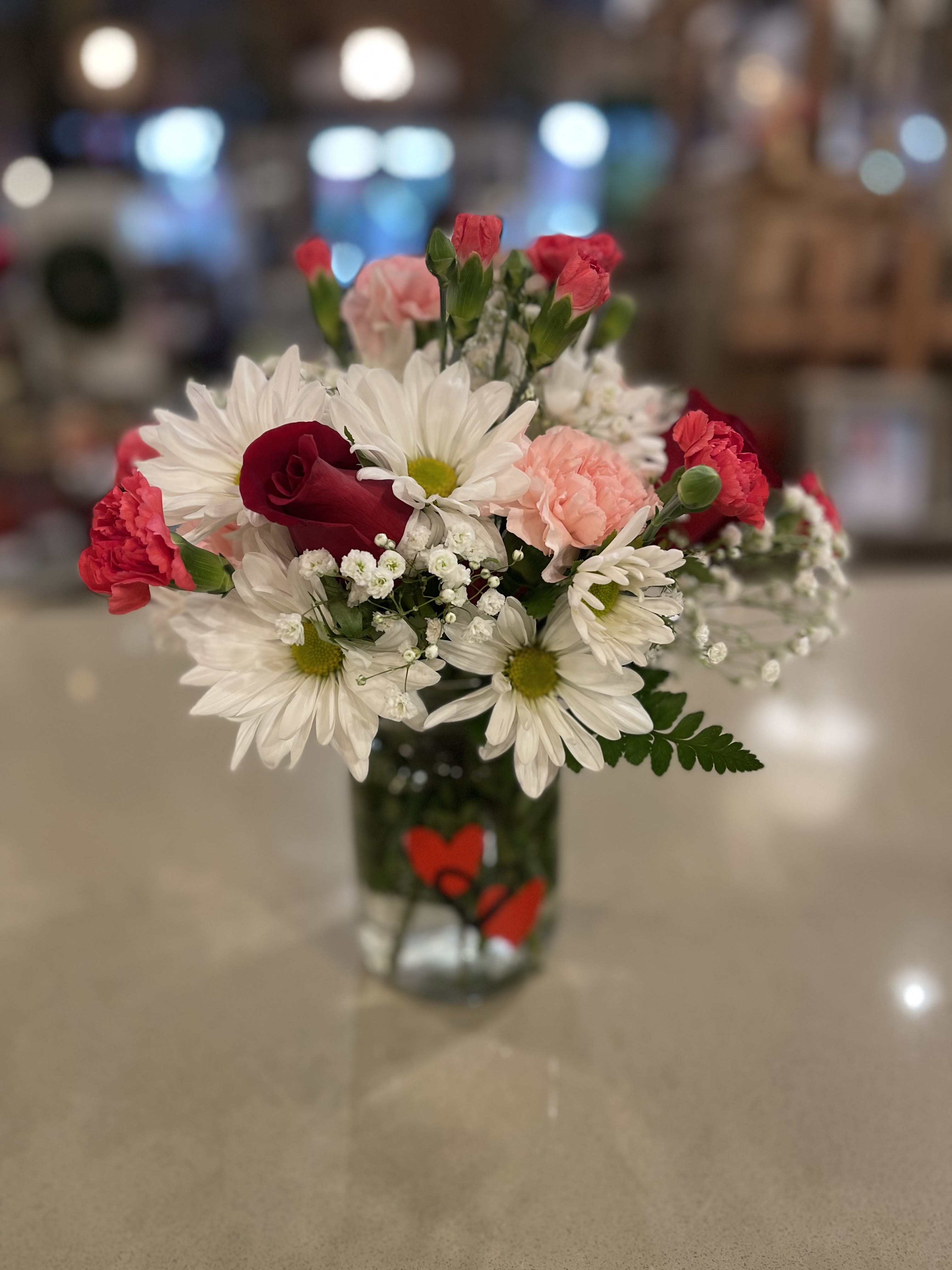 Bouquet of white daisies, red roses, and pink carnations in a glass vase