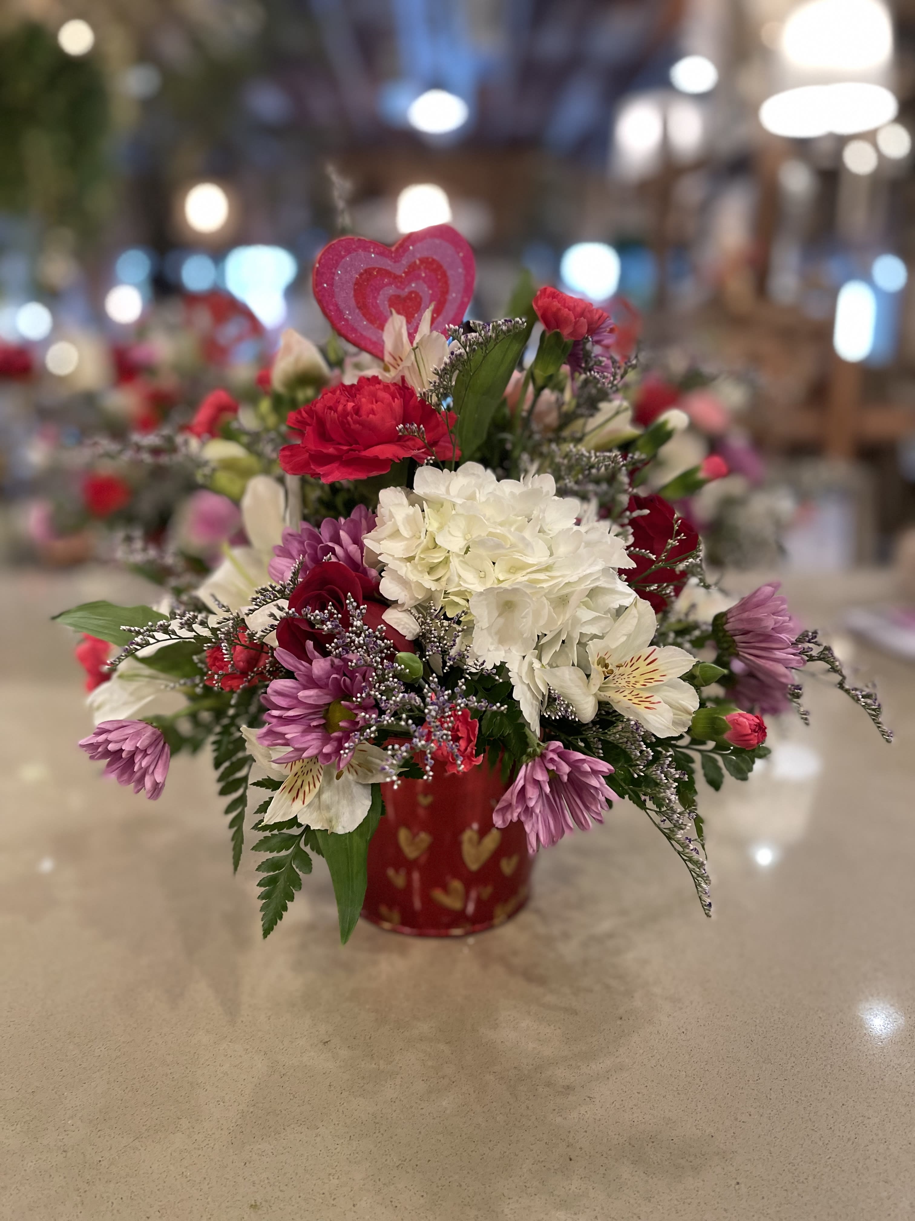 Mixed pink, white, and purple flowers in a red heart-patterned container