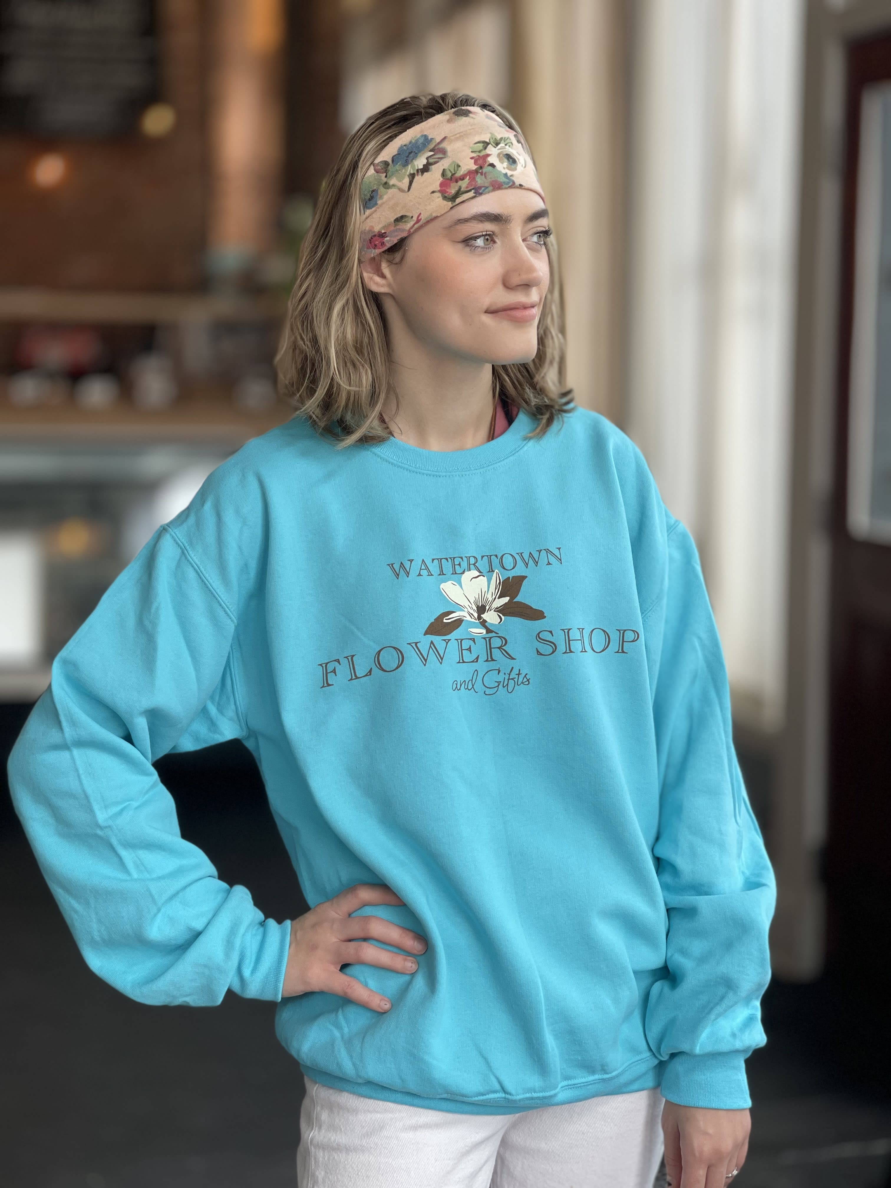 Woman wearing a turquoise flower shop sweatshirt and floral headband