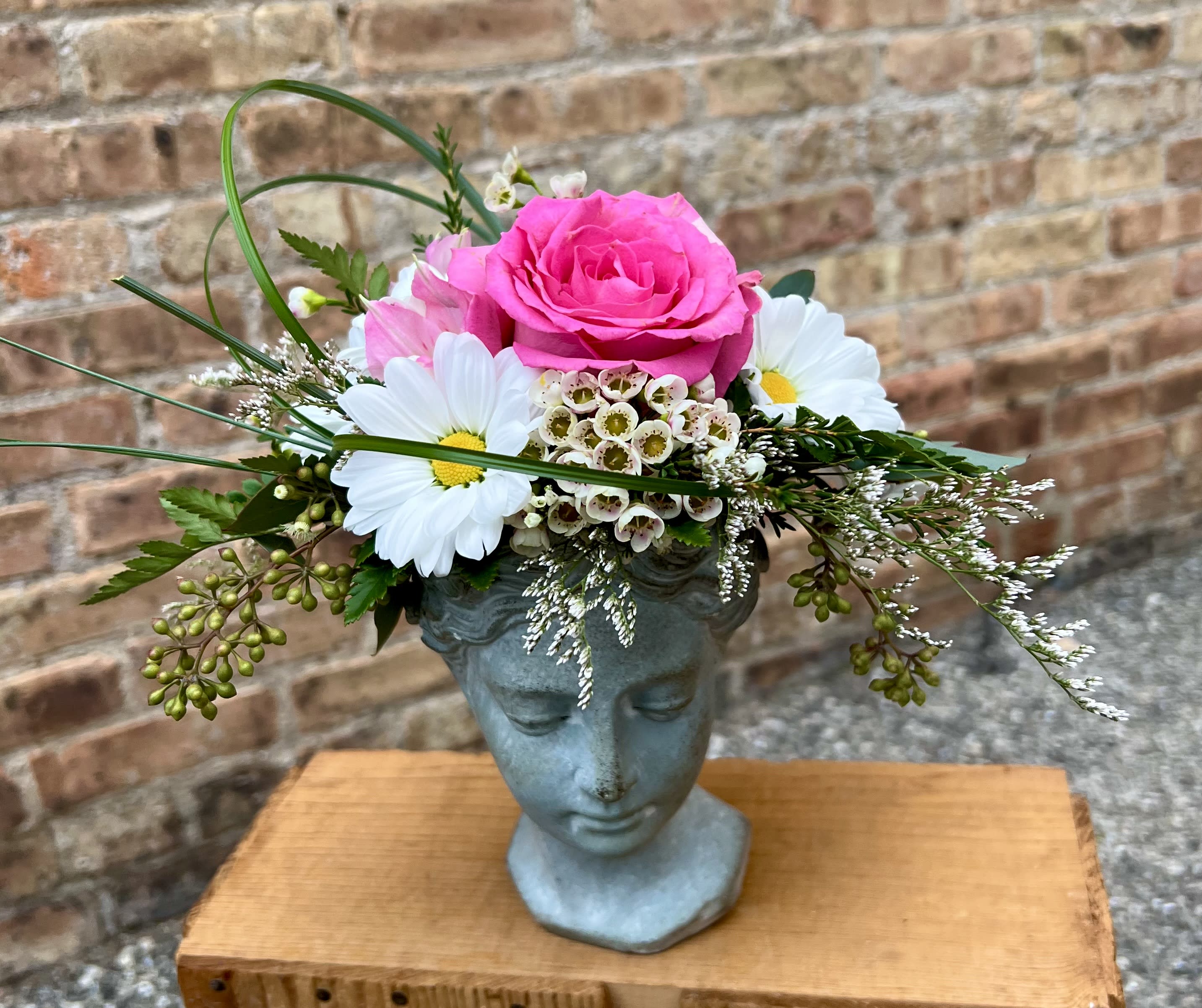 Pink rose arrangement in a blue face-shaped vase with white daisies