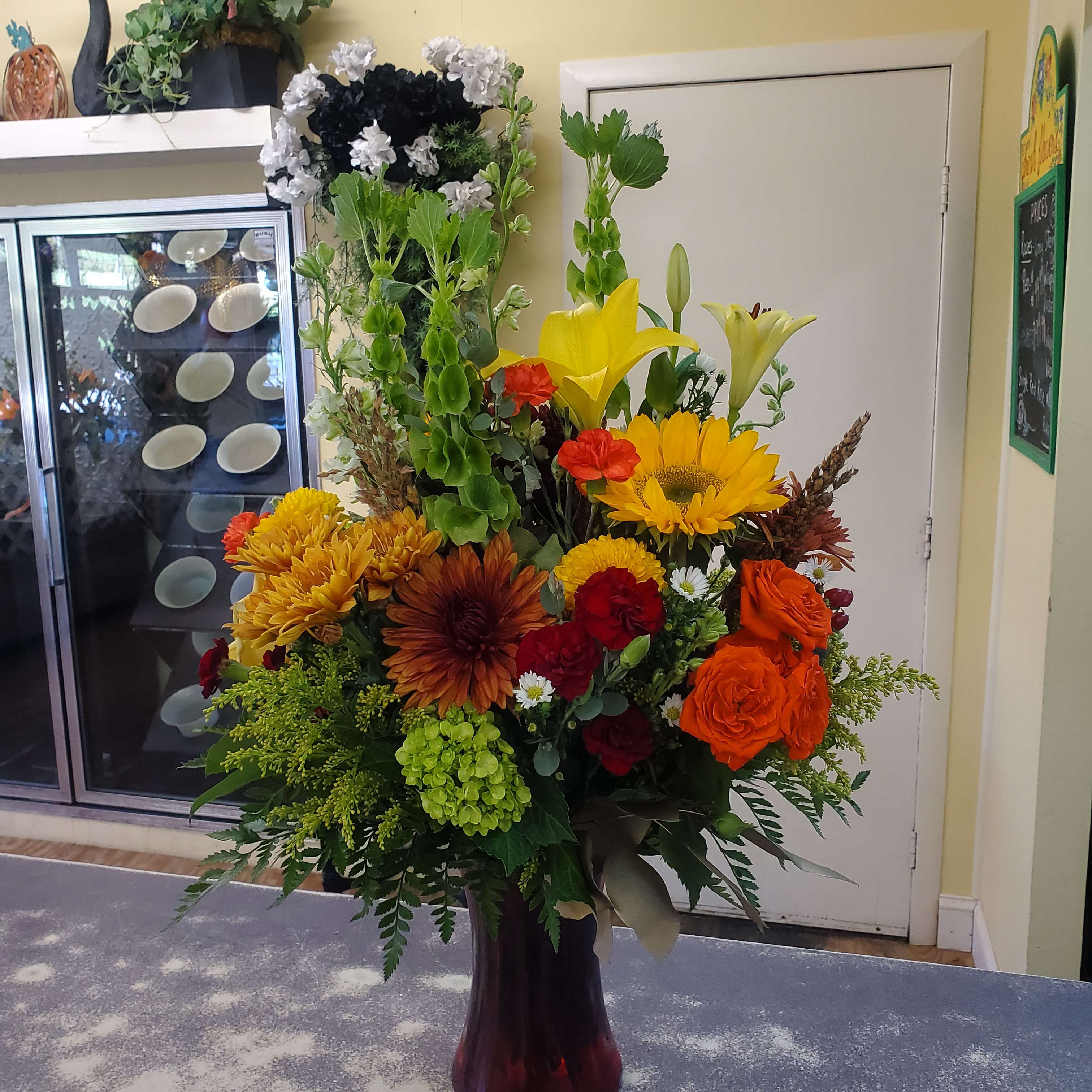 Tall mixed bouquet in a dark vase with lilies, roses, and sunflowers