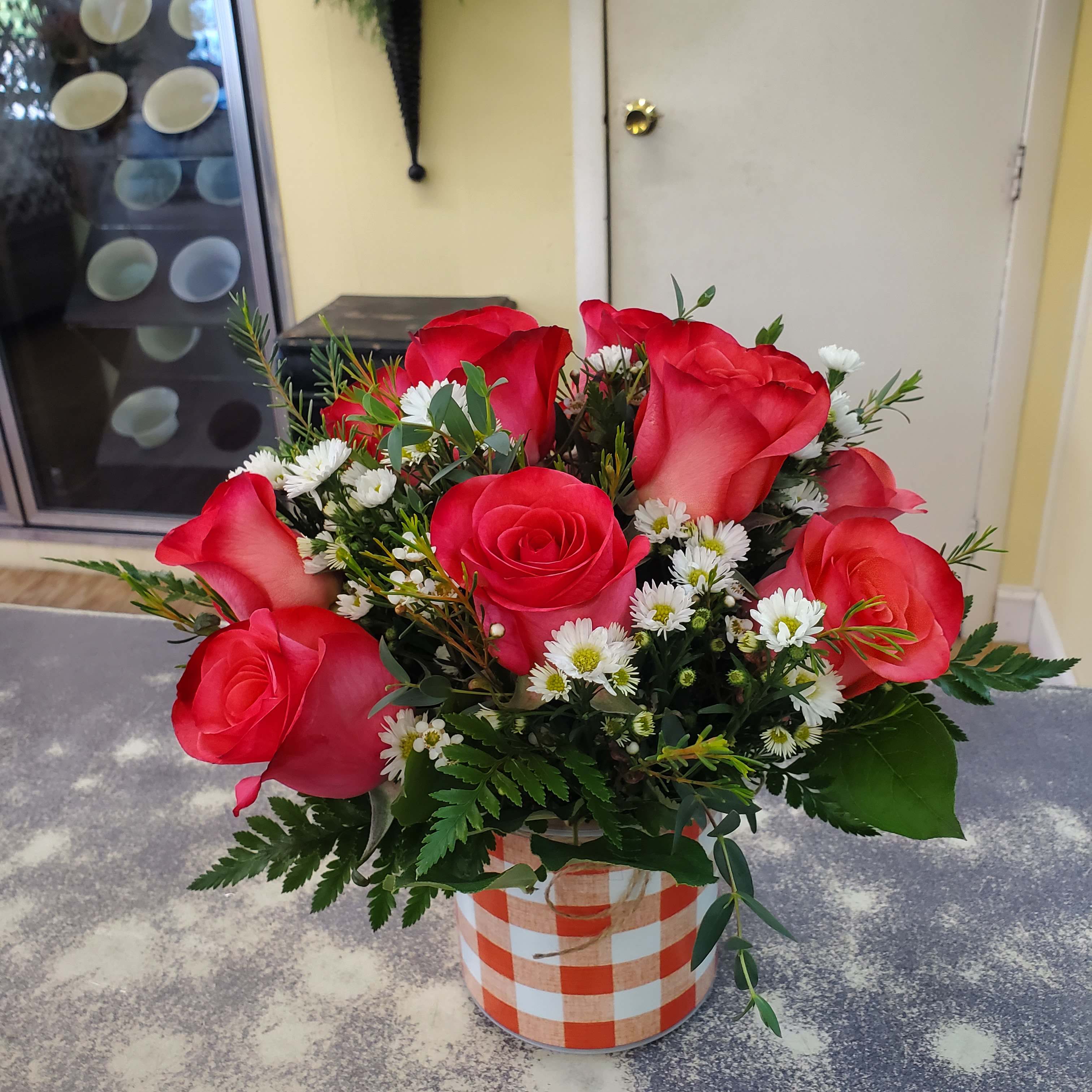 Bouquet of red roses and white daisies in a checkered container