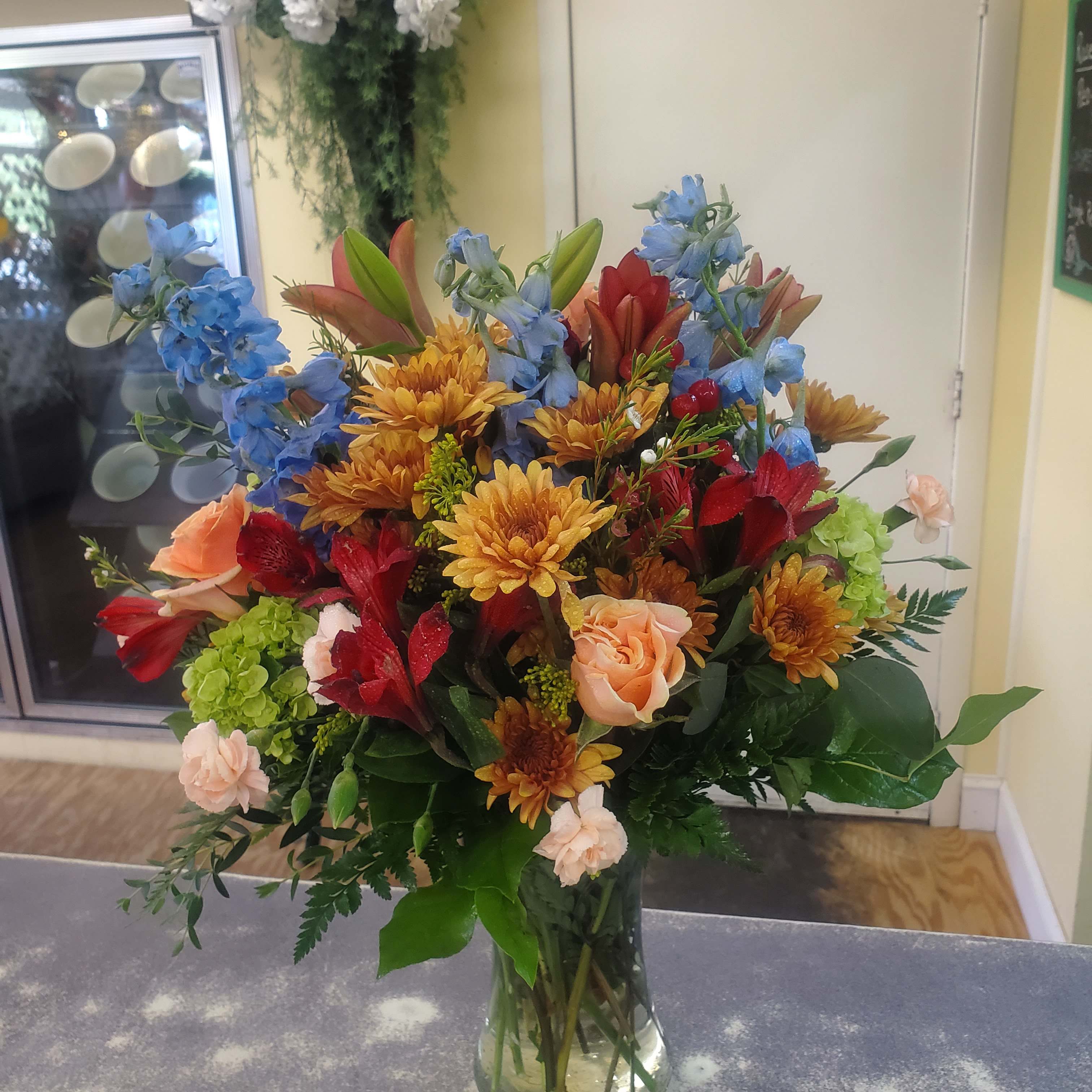 Mixed bouquet in a clear glass vase with blue, red, peach, and gold flowers