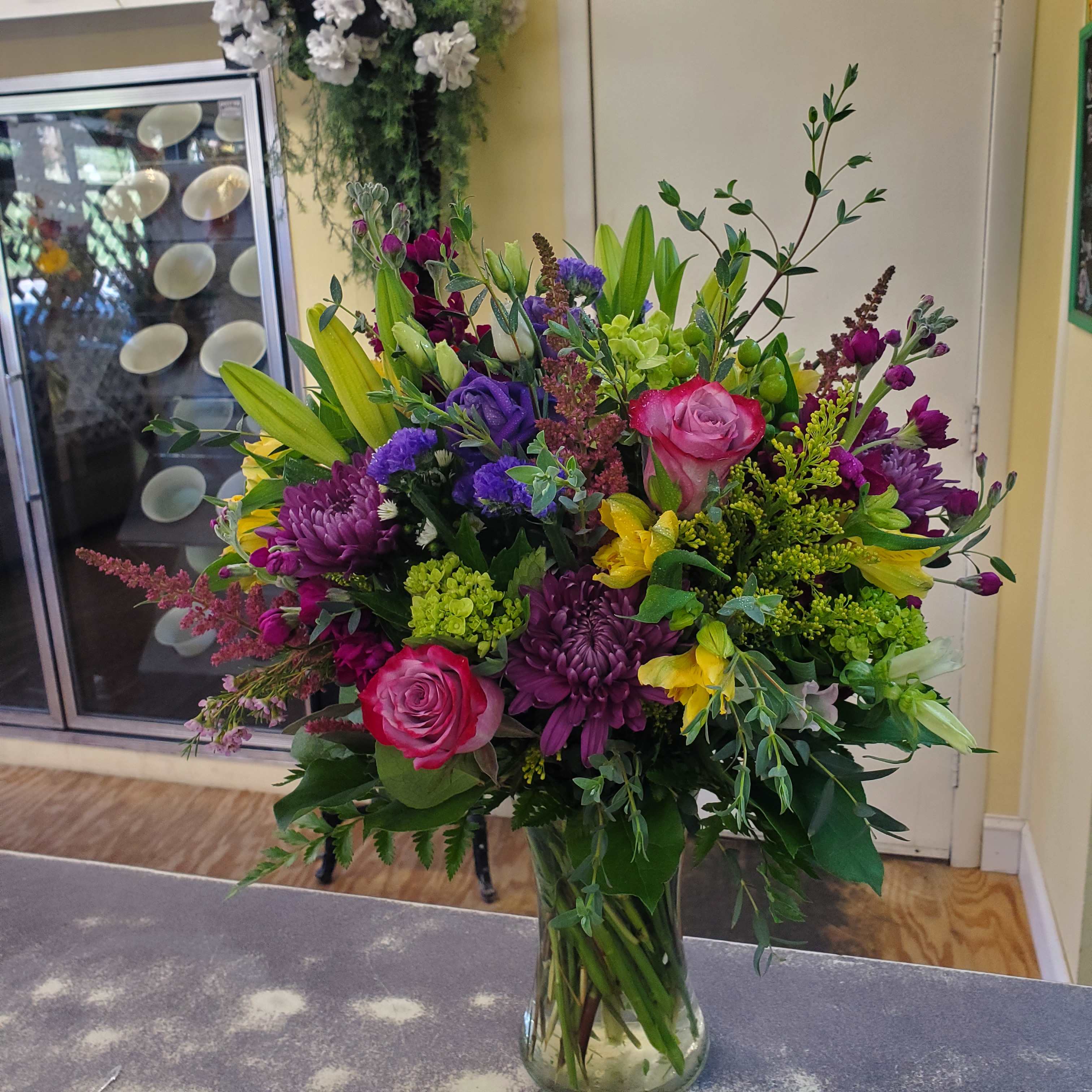 Mixed bouquet of pink roses, purple mums, and yellow lilies in a glass vase