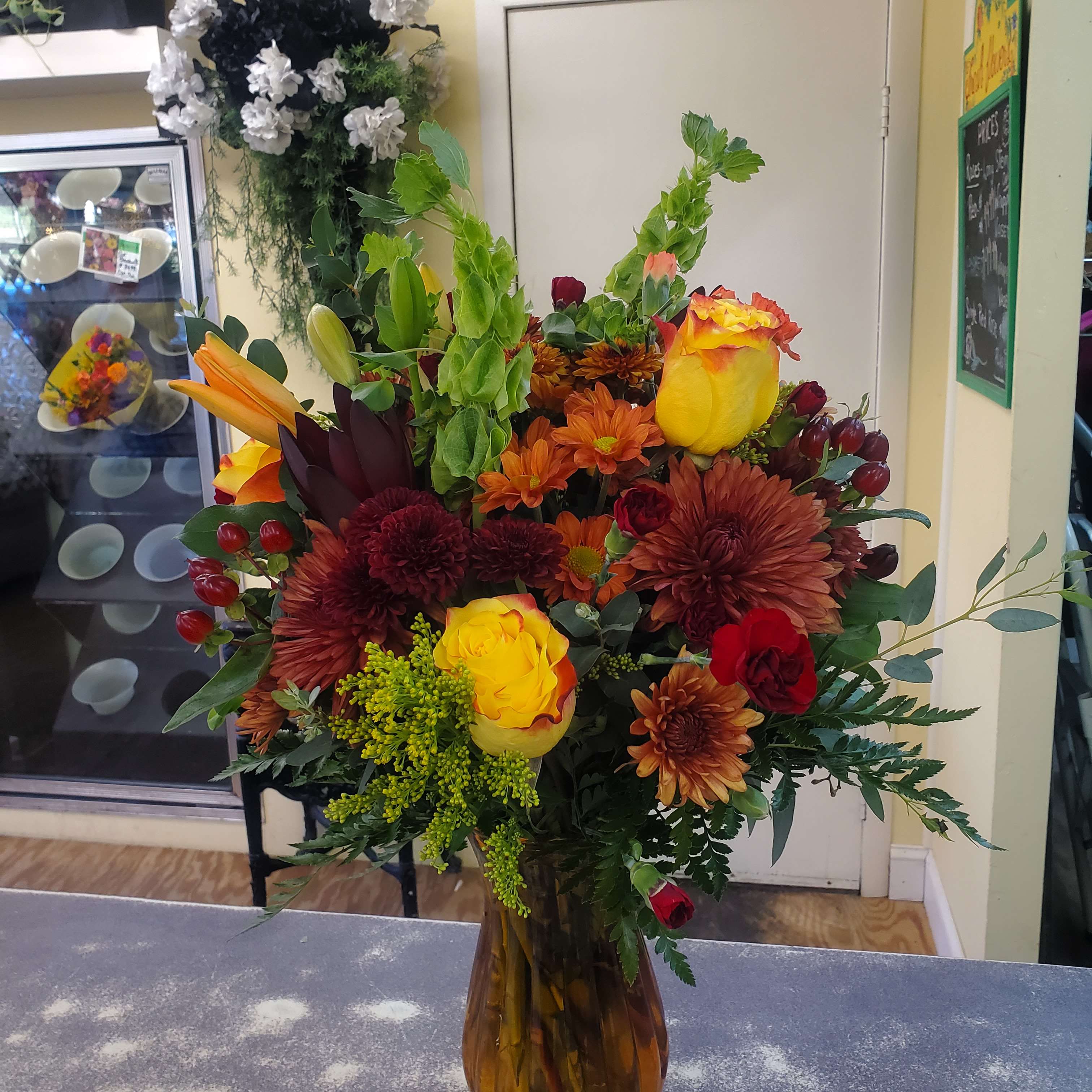 Mixed bouquet of yellow roses, orange lilies, and burgundy mums in a glass vase