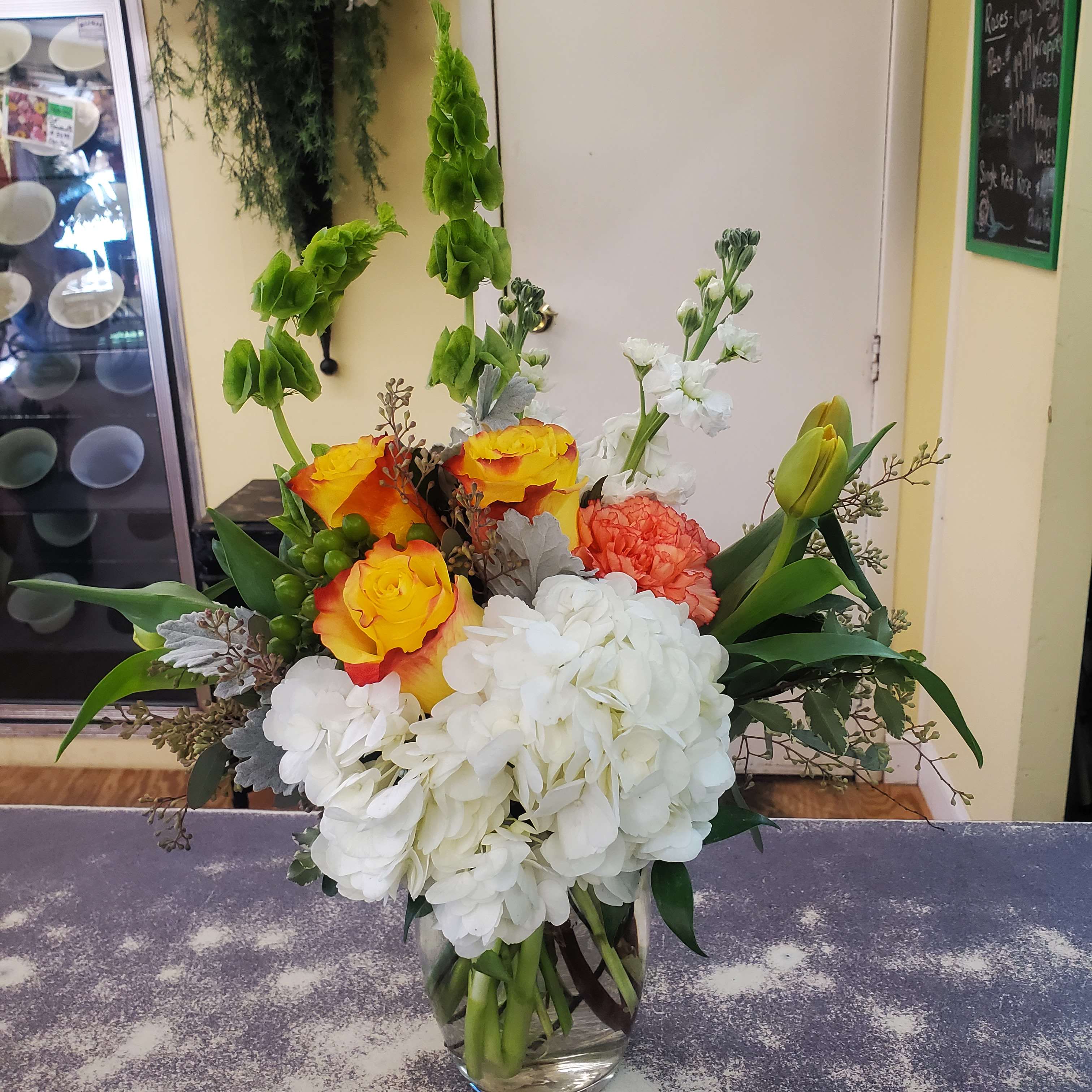 Colorful bouquet with white hydrangeas, yellow roses, and green tulips in a glass vase