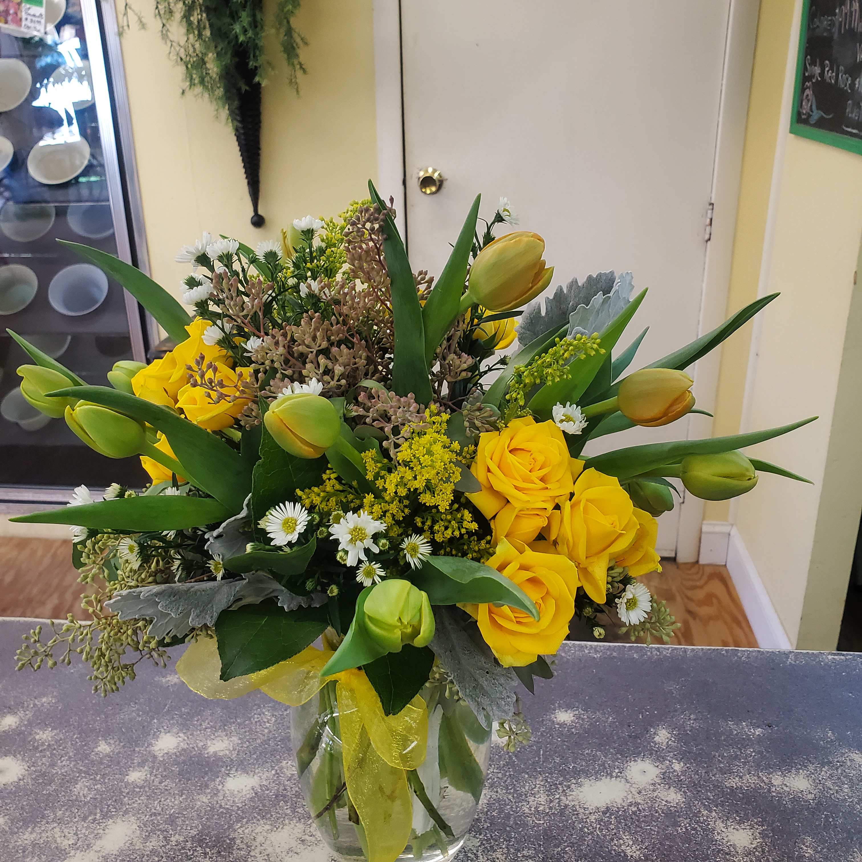 Yellow roses and tulips in a clear glass vase with small white daisies