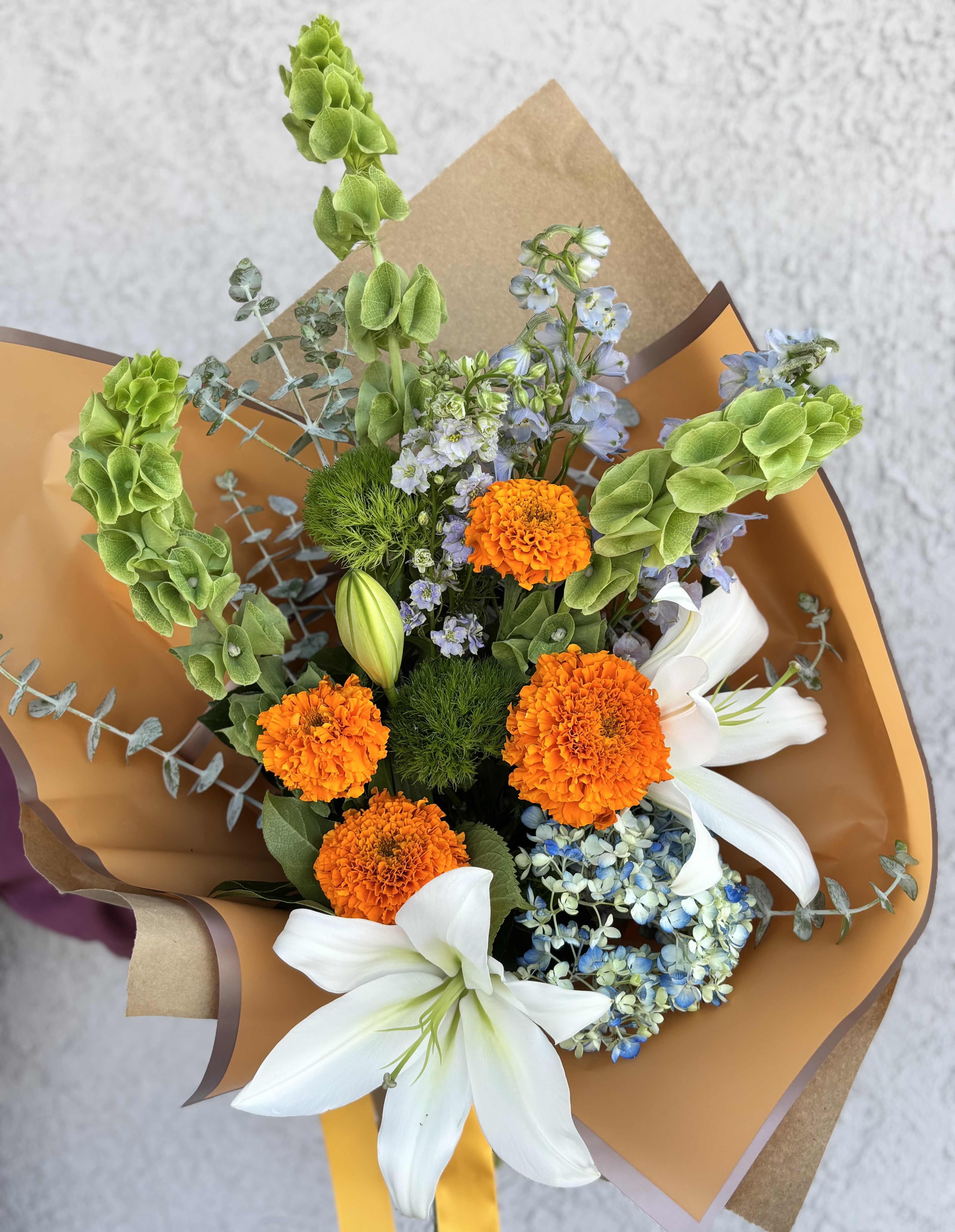 Bouquet of orange marigolds, white lilies, and blue flowers wrapped in brown paper
