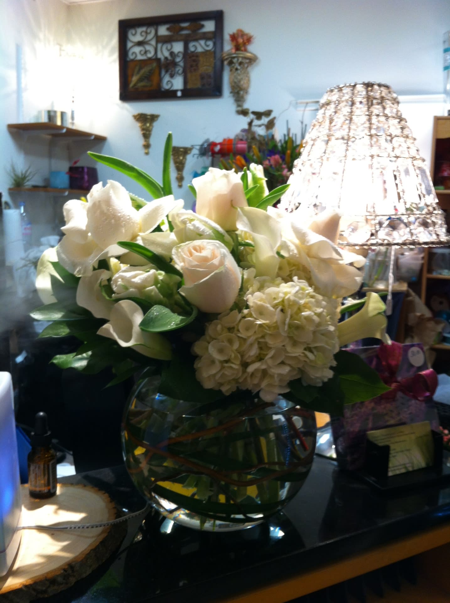 White floral arrangement in a round glass vase with calla lilies and roses