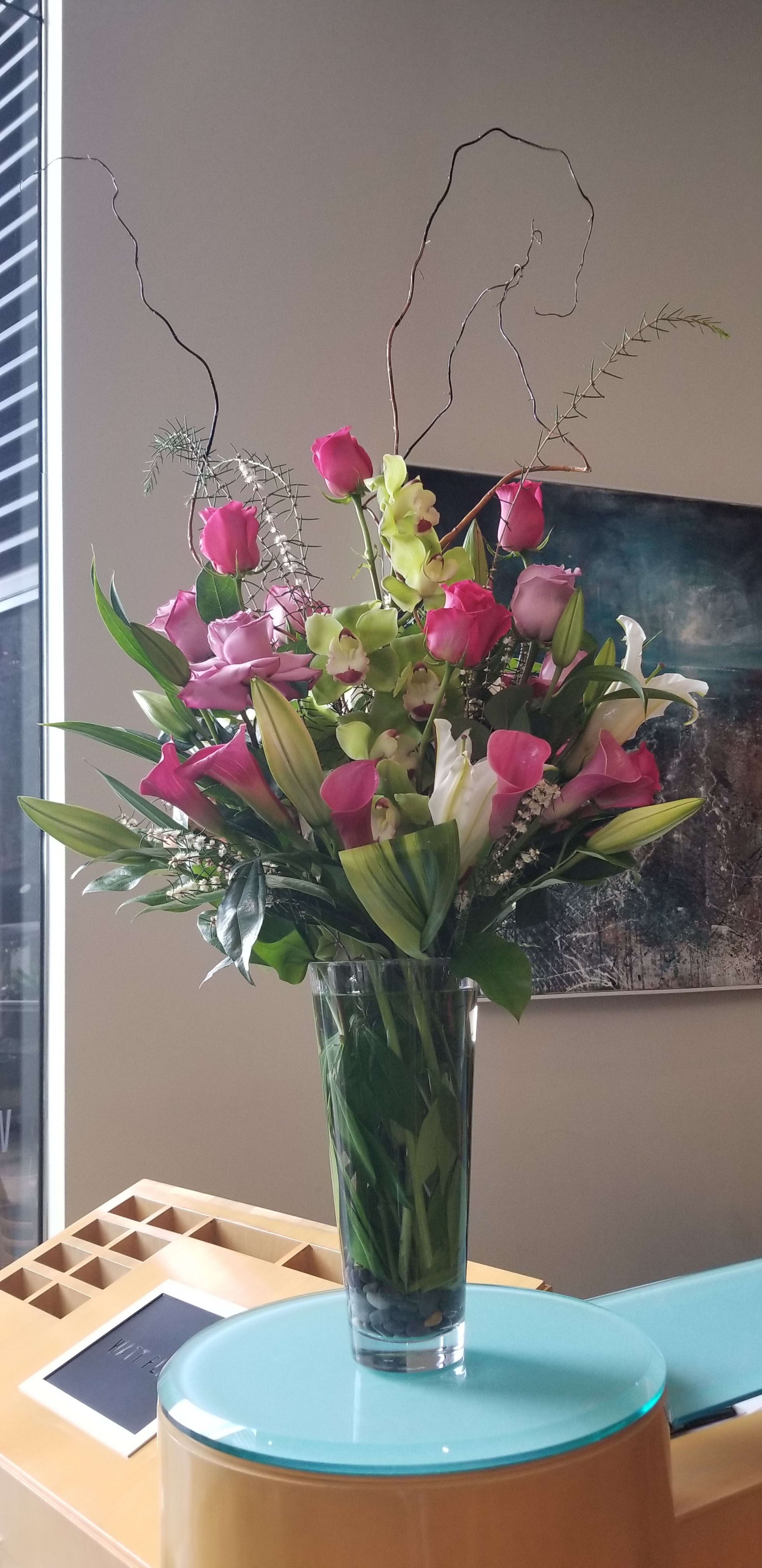 Tall bouquet of pink roses, calla lilies, and green orchids in a glass vase