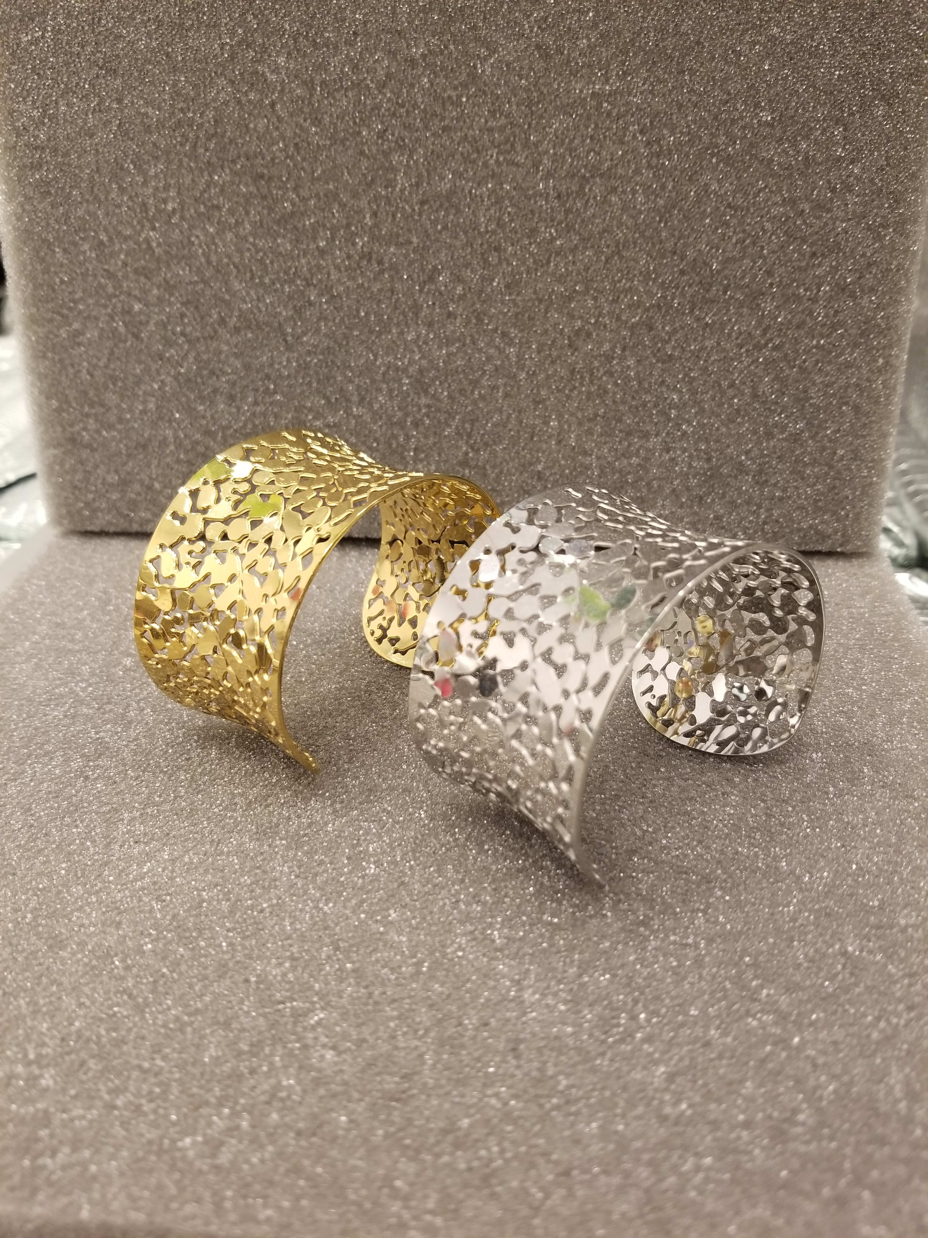 Two decorative metal cuff bracelets on a glittery gray surface