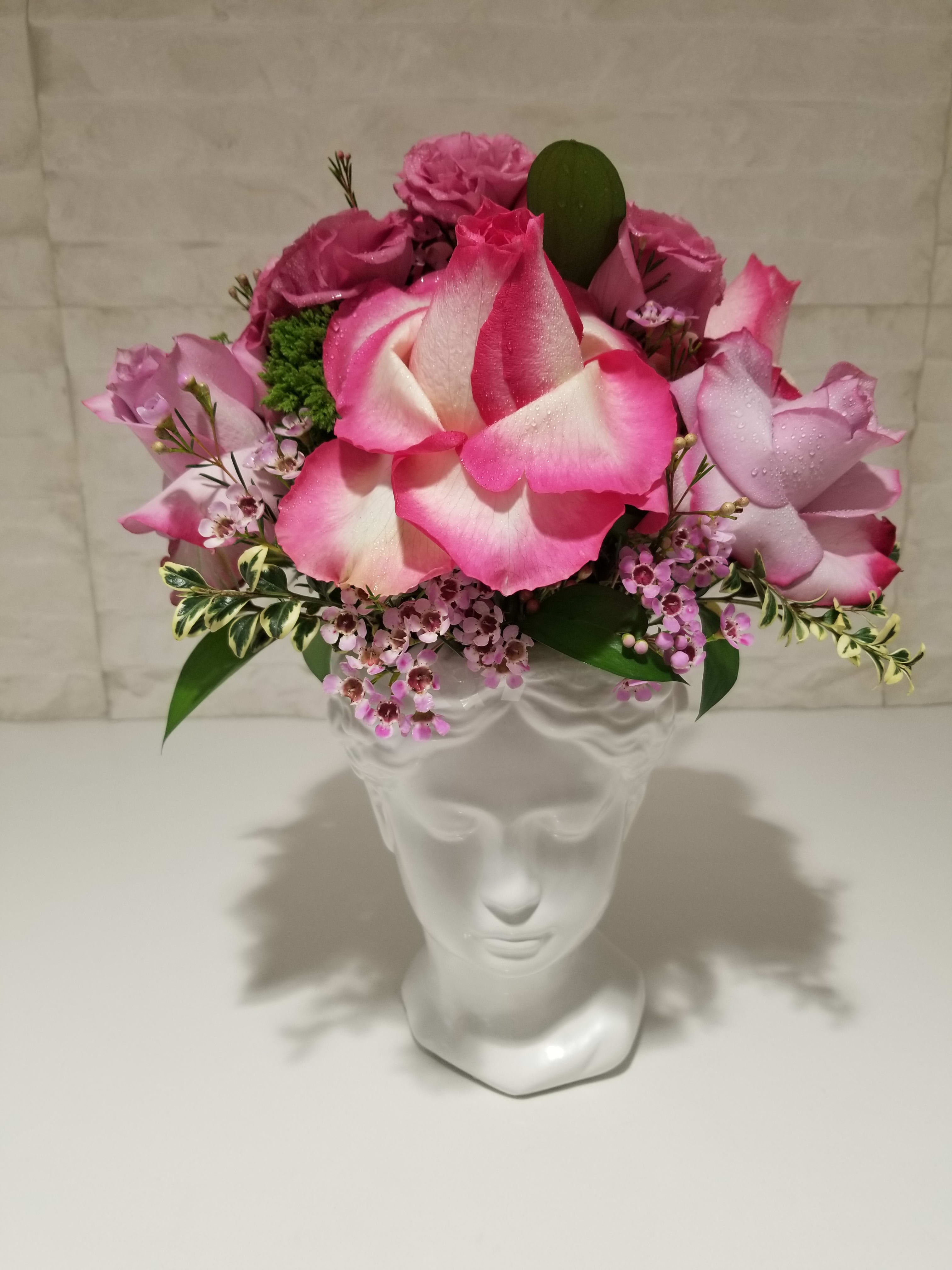 Pink and white rose arrangement in a clear glass vase shaped like a face