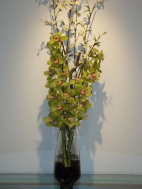 Tall floral arrangement with green orchids in a glass vase