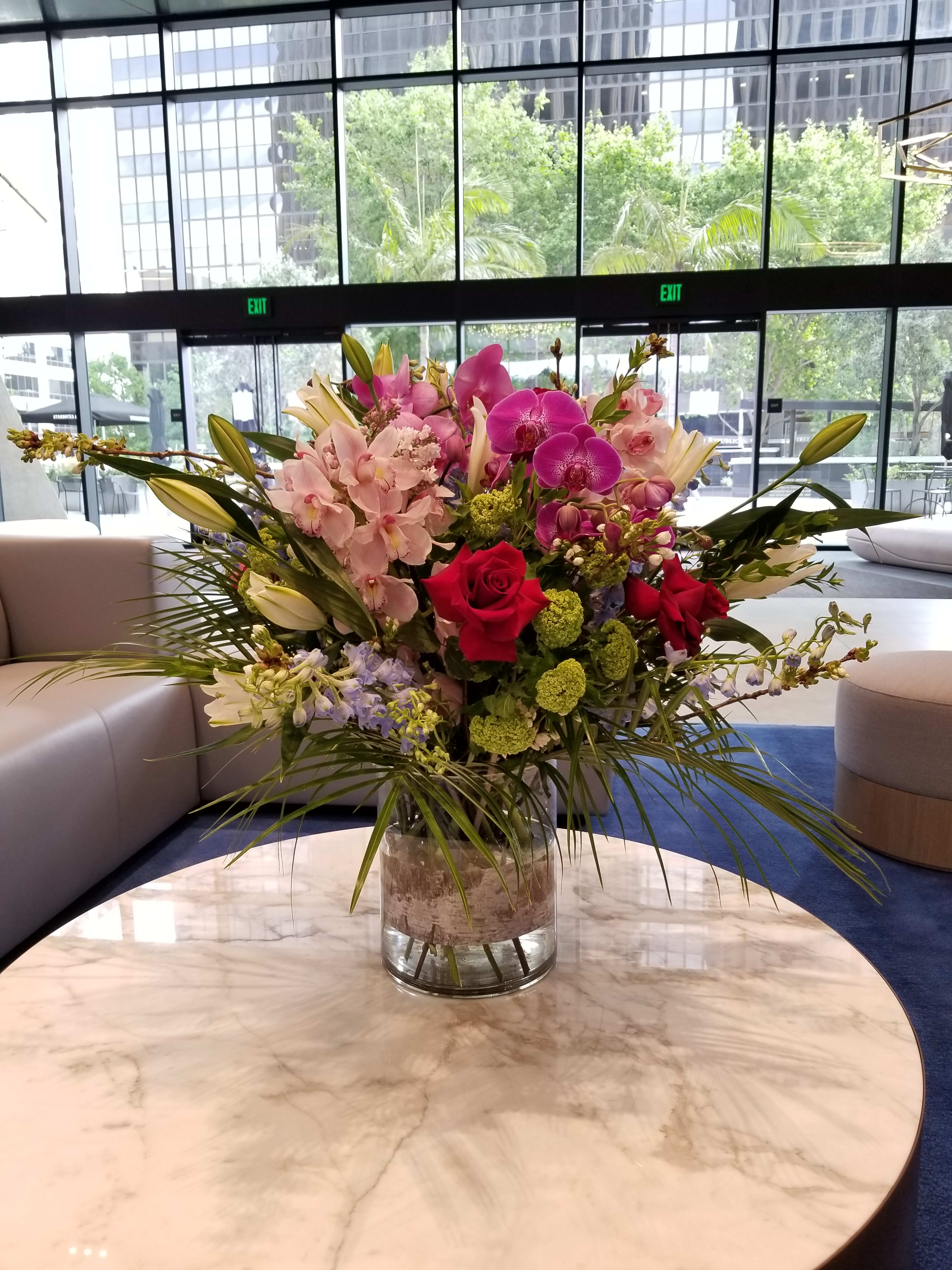 Large mixed bouquet in a clear glass vase with pink orchids and red roses