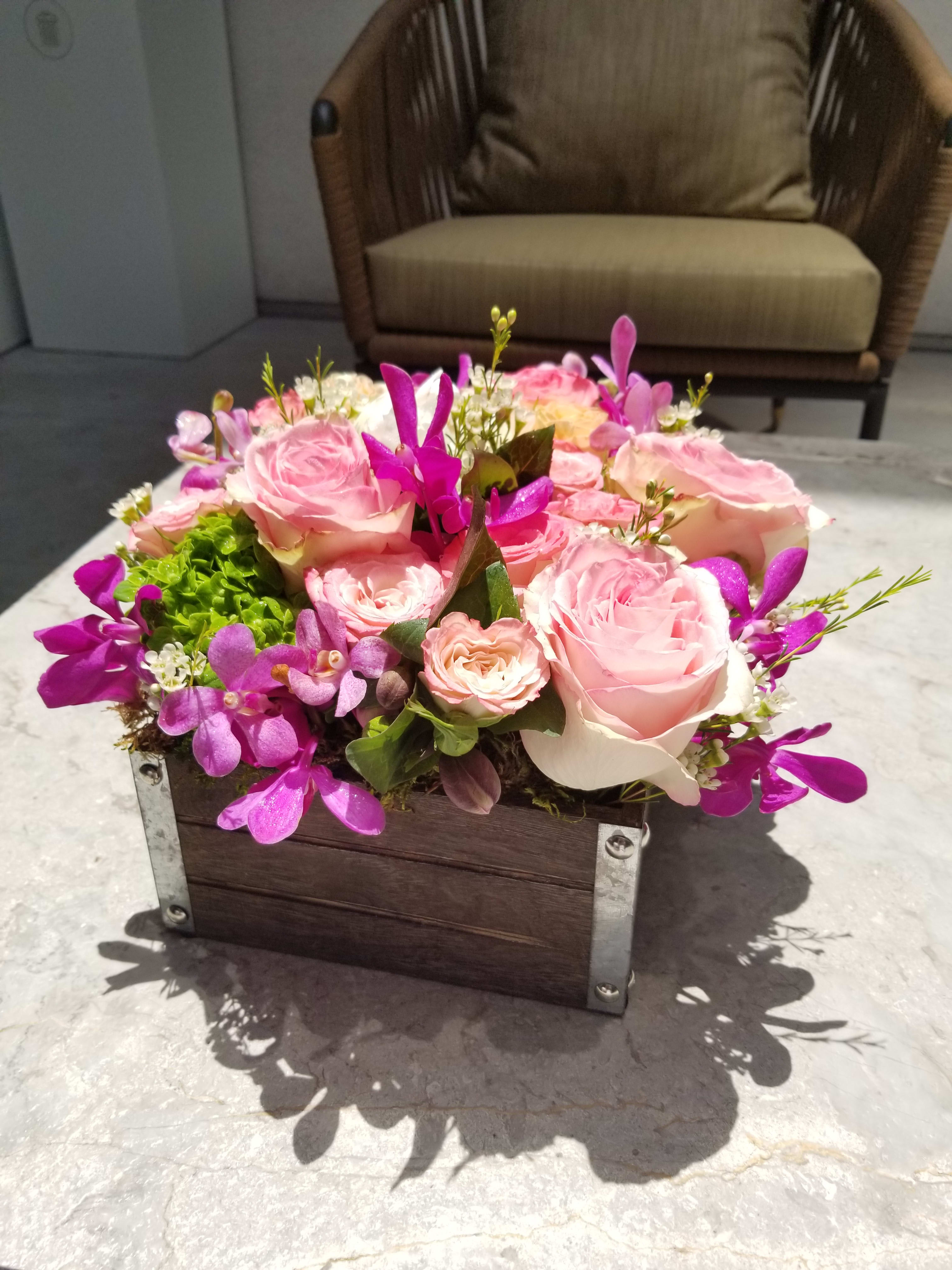 Pink roses and purple orchids arranged in a wooden box