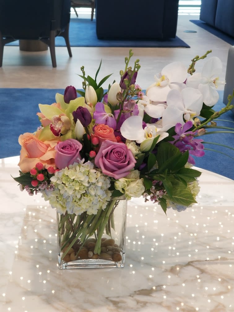Mixed bouquet of roses, orchids, tulips, and hydrangeas in a glass vase