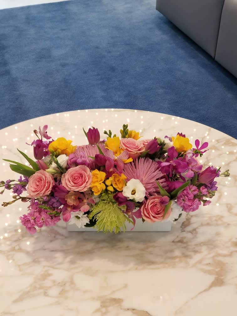 Mixed pink, purple, and yellow floral arrangement in a low white container
