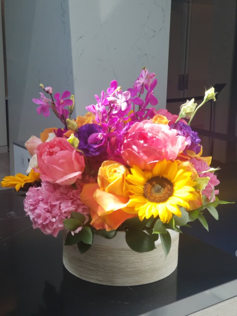 Bright mixed bouquet in a round box with sunflowers, roses, and orchids
