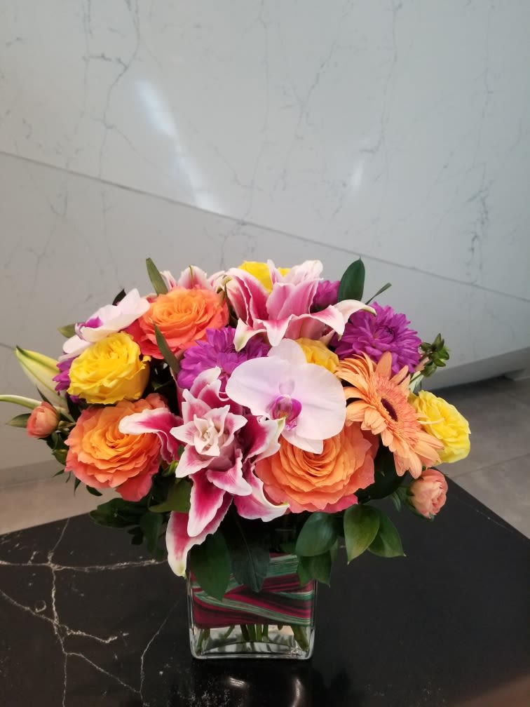 Colorful bouquet of roses, lilies, orchids, and daisies in a glass vase