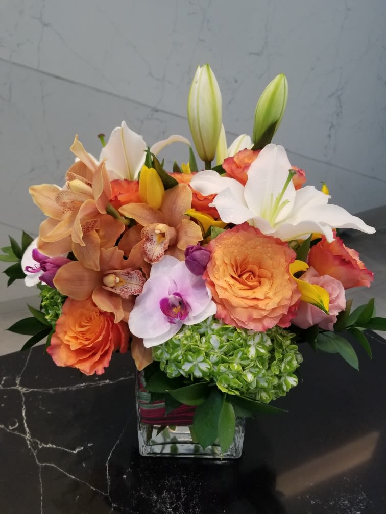Mixed bouquet of orange roses, orchids, lilies, and hydrangea in a glass vase