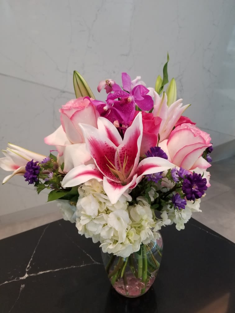 Pink lilies and roses with purple orchids in a glass vase