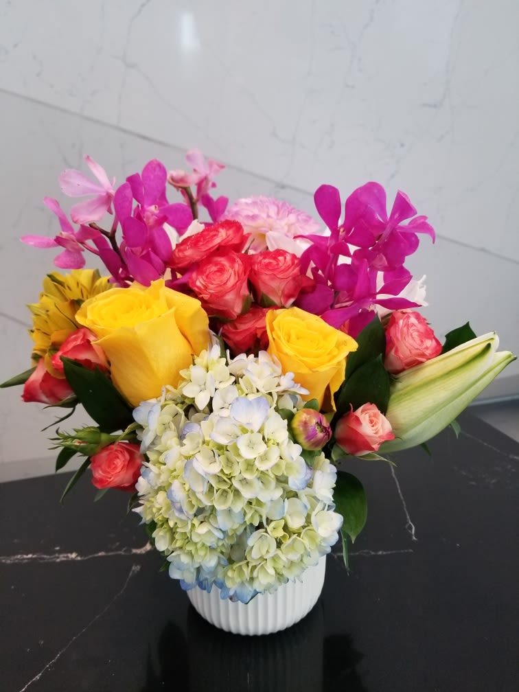 Colorful bouquet with roses, hydrangea, orchids, and lilies in a white vase