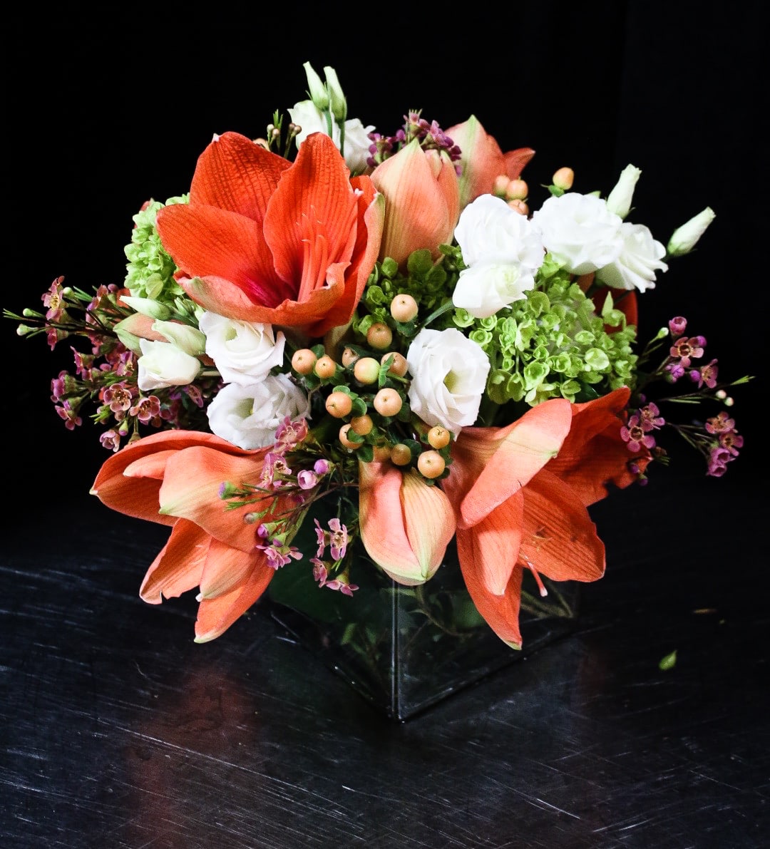 Orange amaryllis and white blooms arranged in a clear glass vase