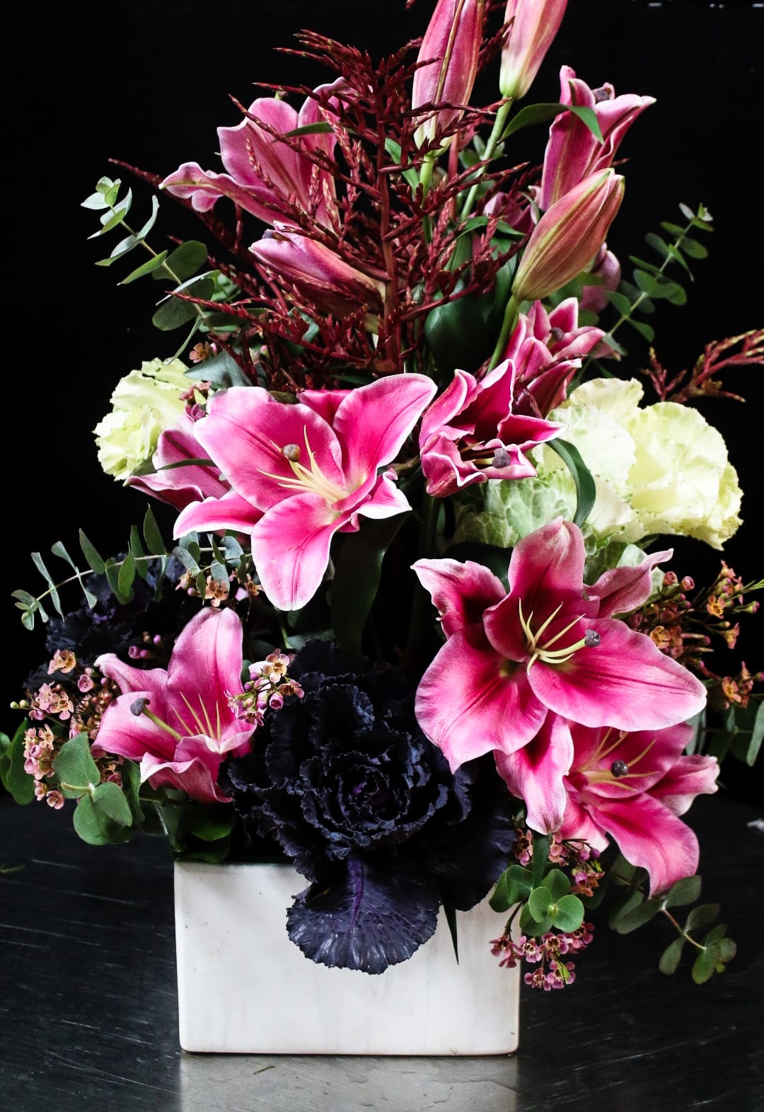Pink lilies and dark purple flowers in a white square vase