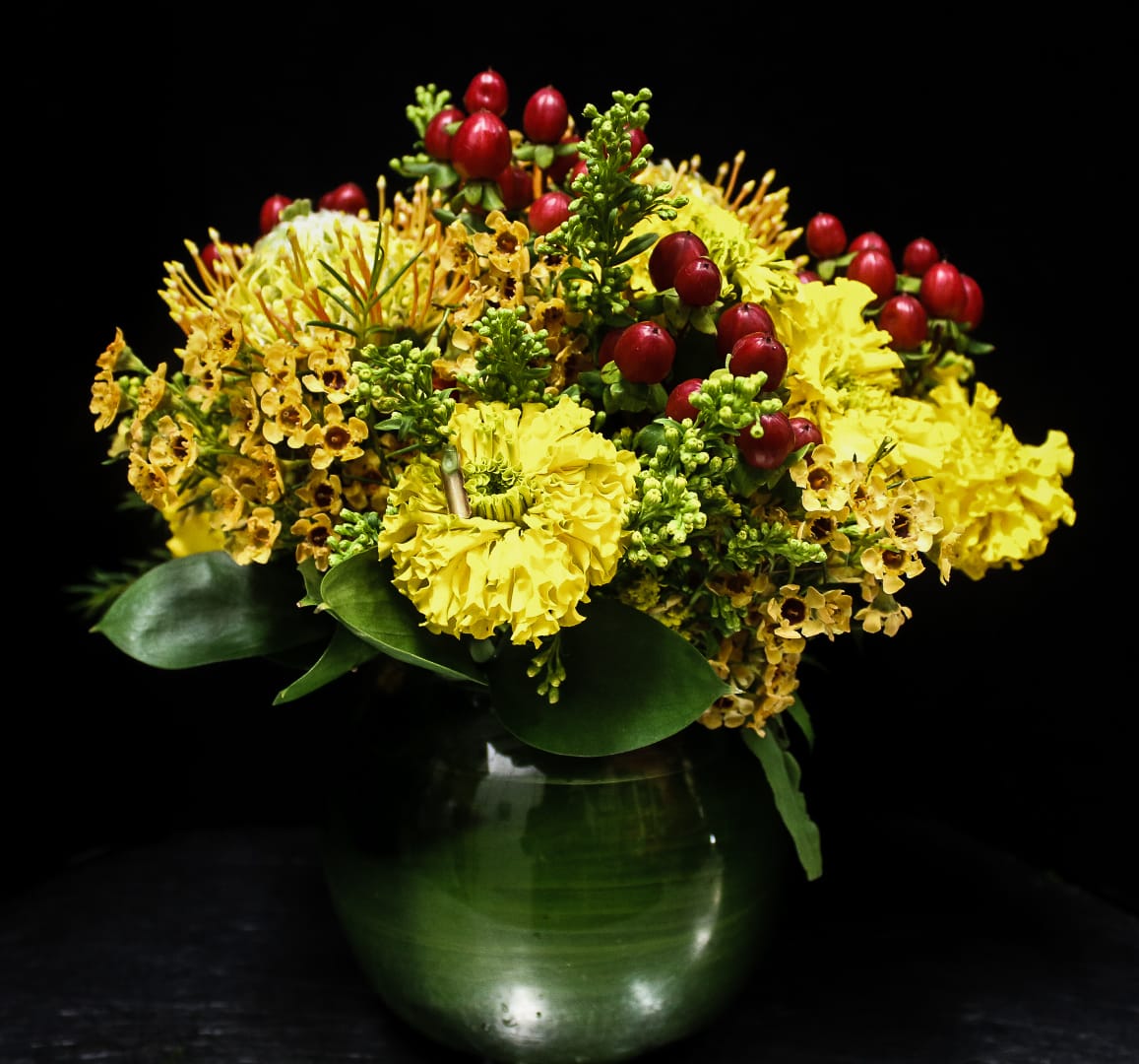 Yellow floral arrangement with red berry accents in a green glass vase