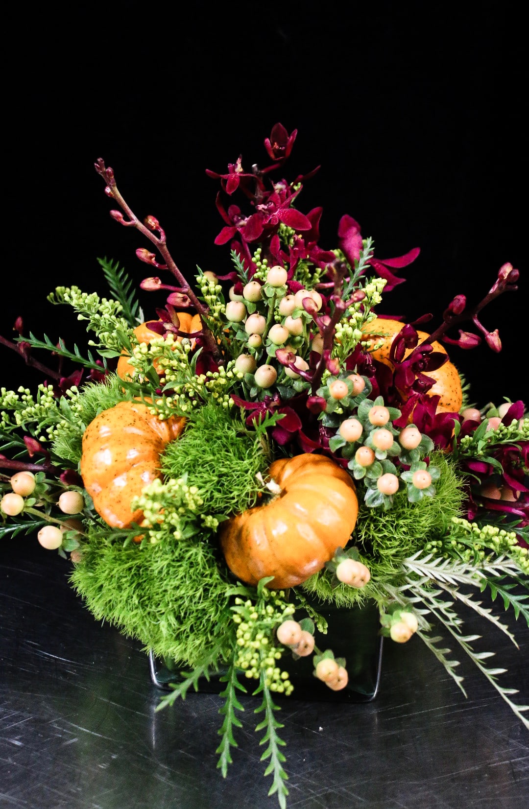 Orange pumpkins in a low floral arrangement with burgundy blooms and berries