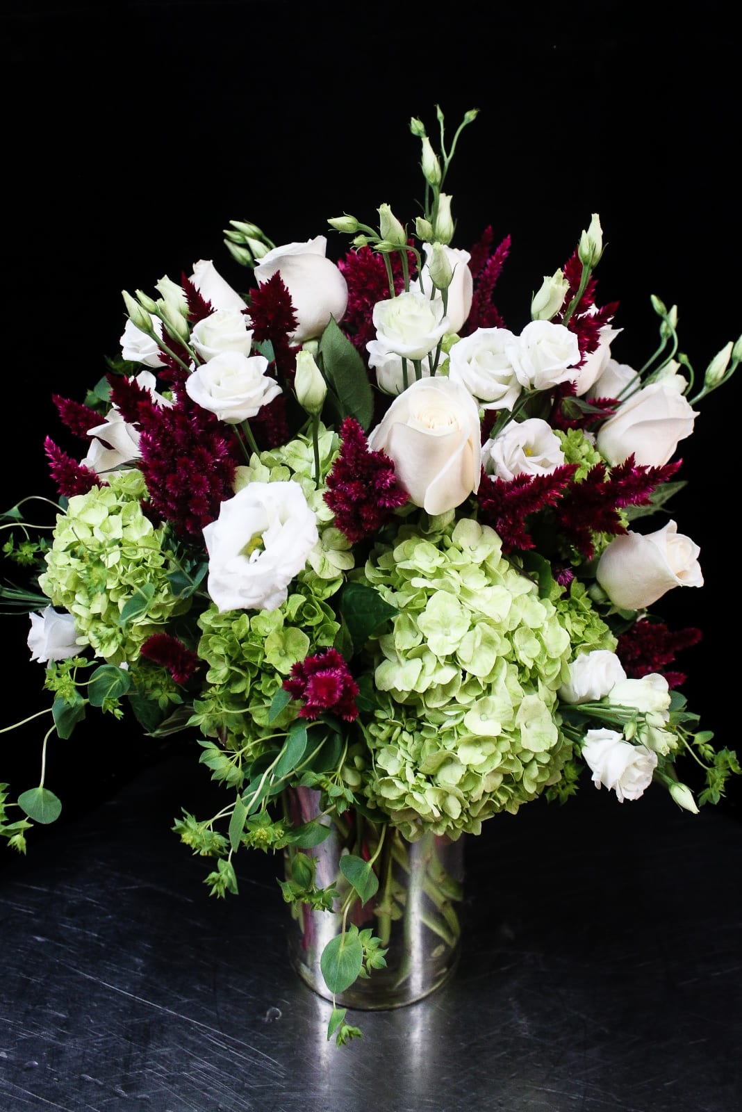 White roses and green hydrangeas in a silver vase with burgundy accents