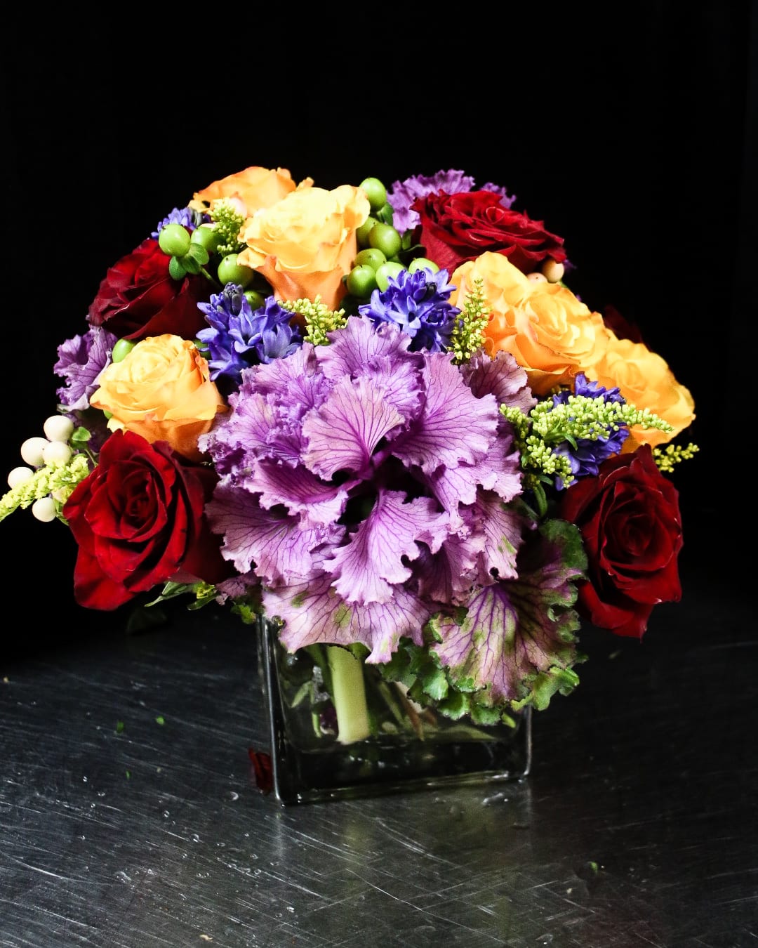 Bouquet of red, orange, and purple flowers in a square glass vase