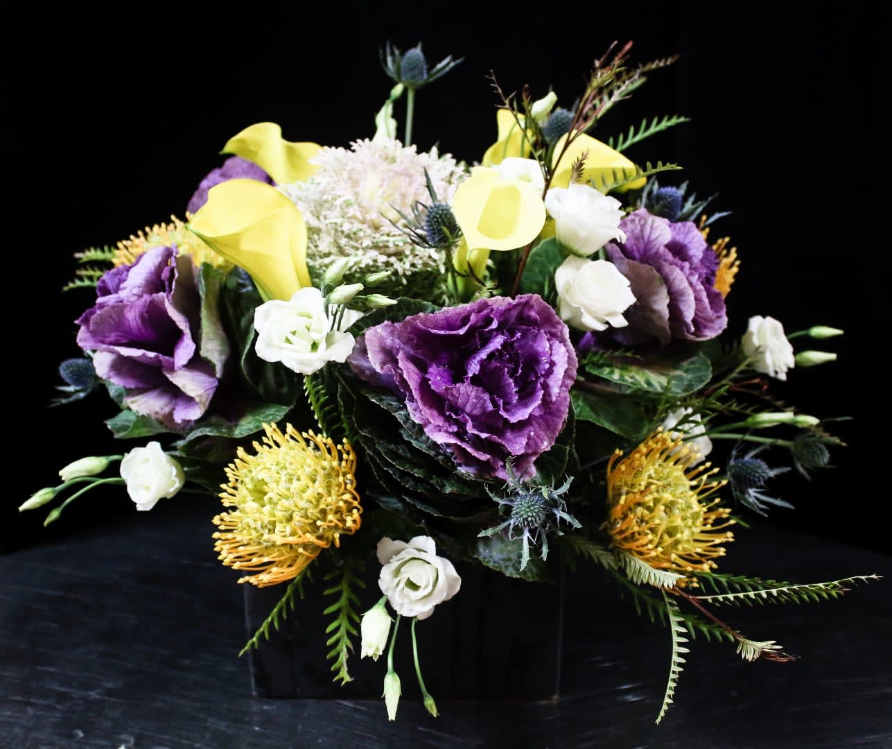 Purple and yellow floral arrangement with white blooms in a black container