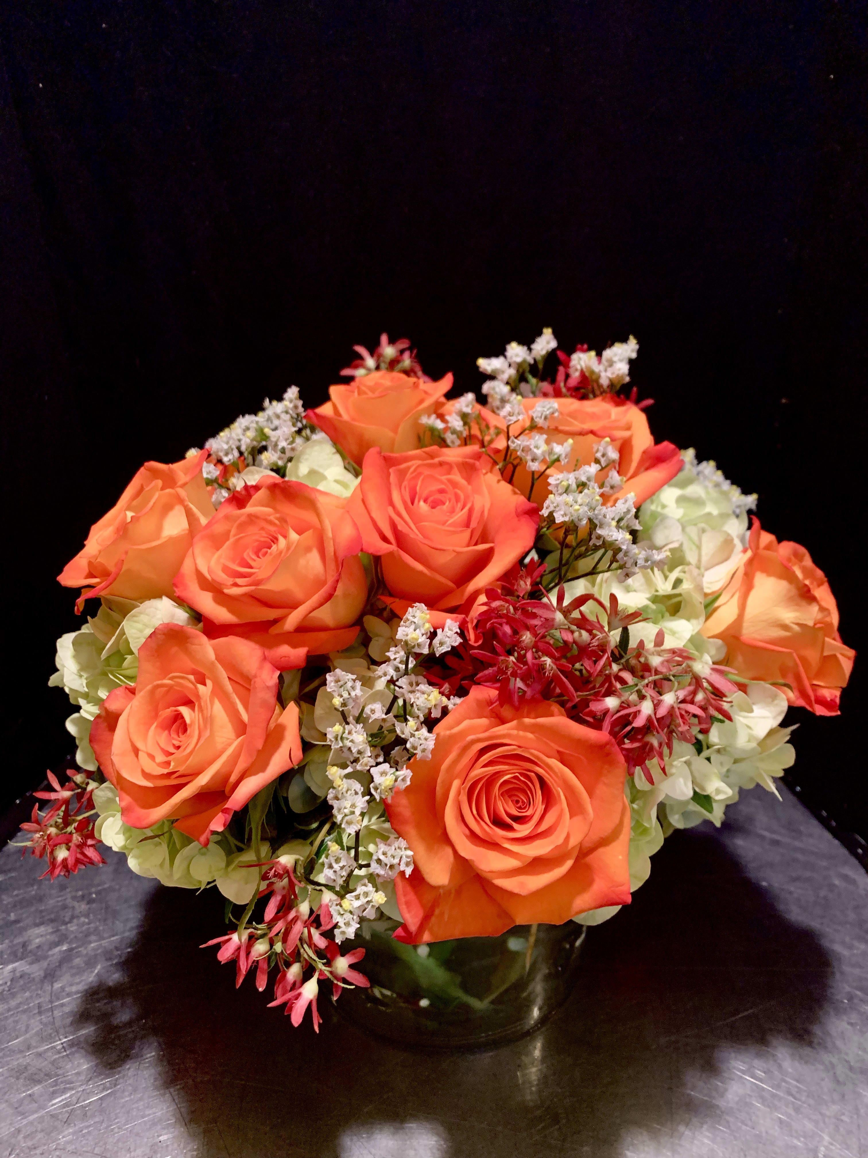Orange roses arranged in a glass vase with white filler flowers