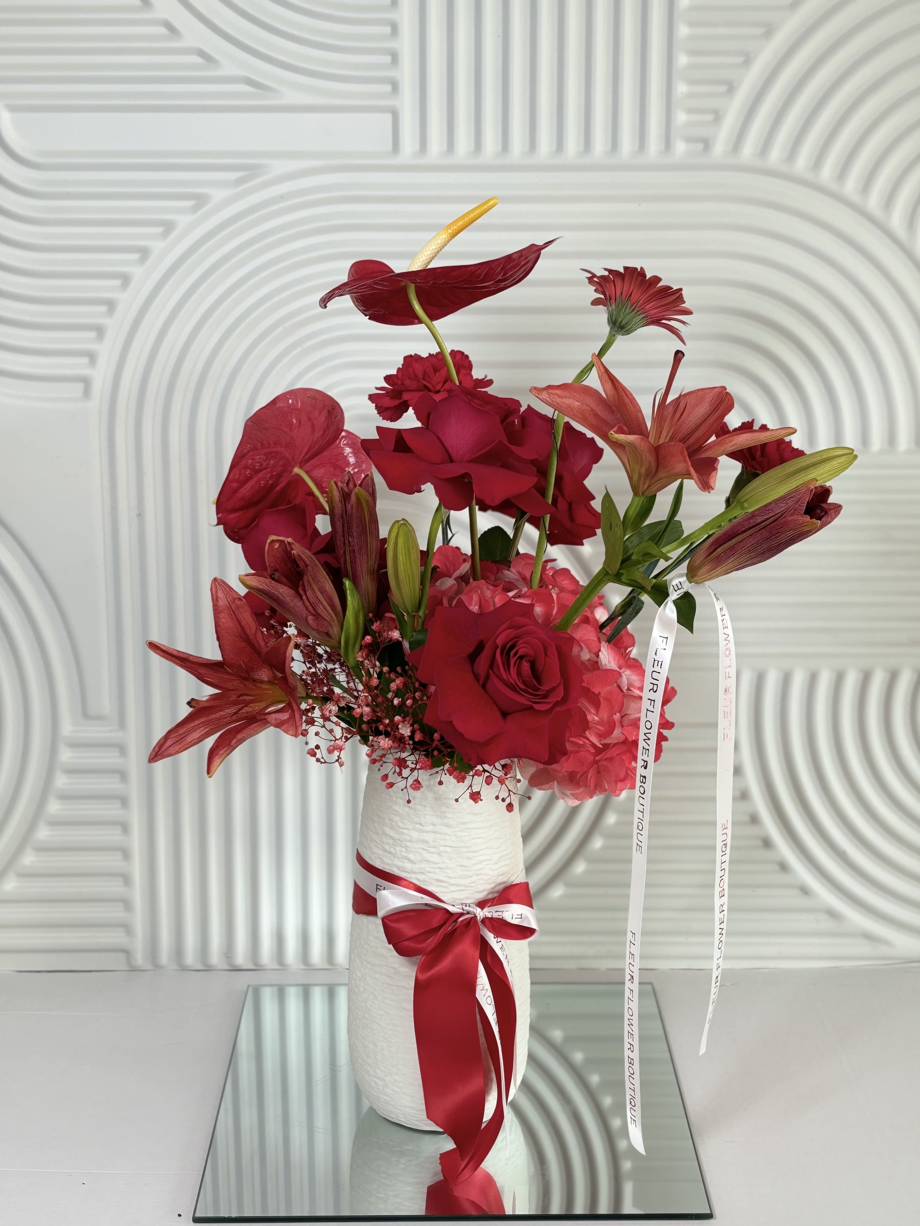 Red floral arrangement in a white vase with a ribbon bow