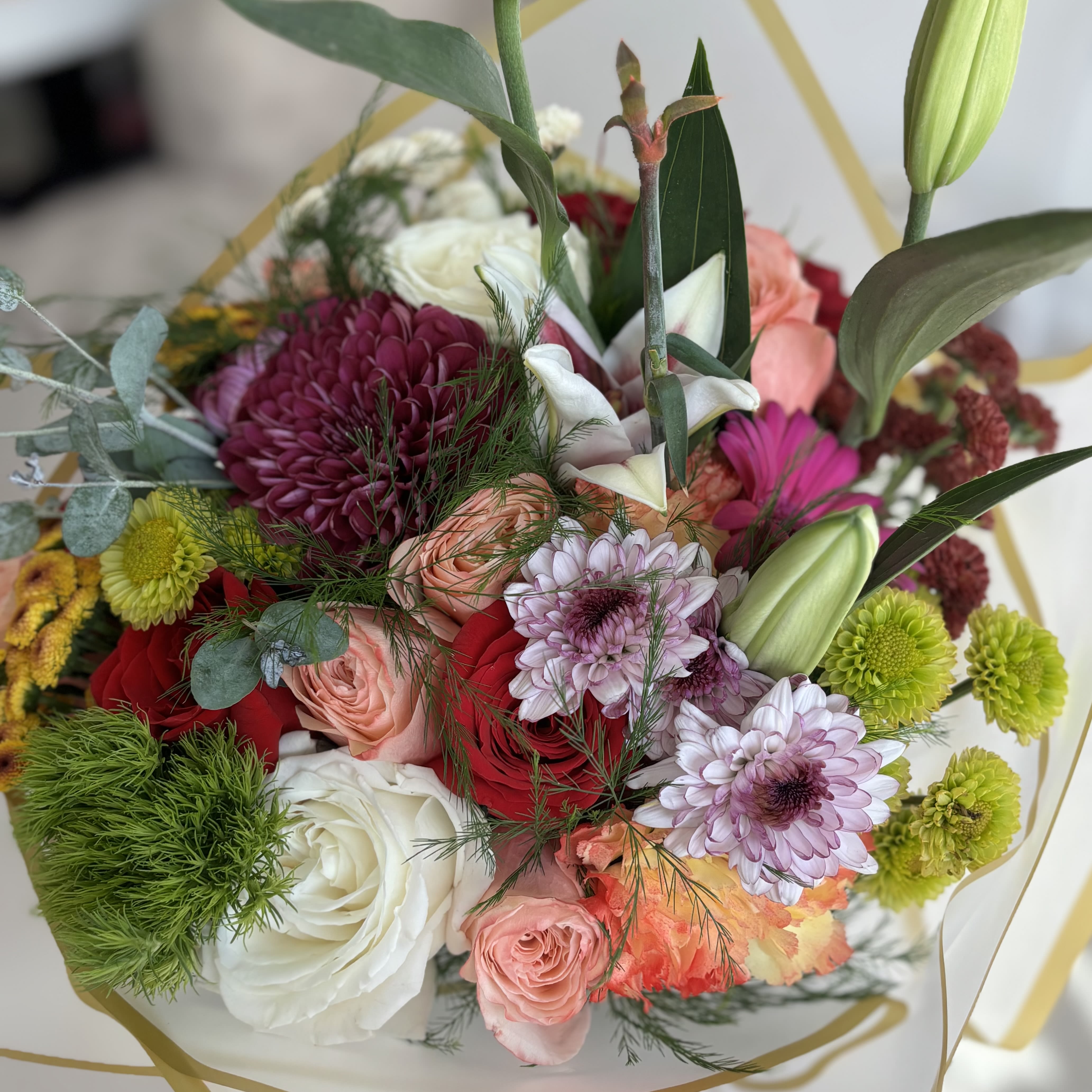 Mixed bouquet of roses, chrysanthemums, and lilies in white wrapping