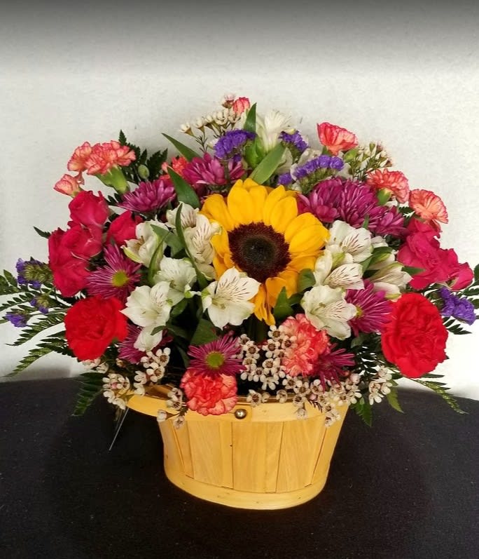 Mixed bouquet in a wooden basket with a sunflower, roses, and white blooms
