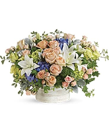 Mixed bouquet of peach roses, white lilies, and blue flowers in a white vase