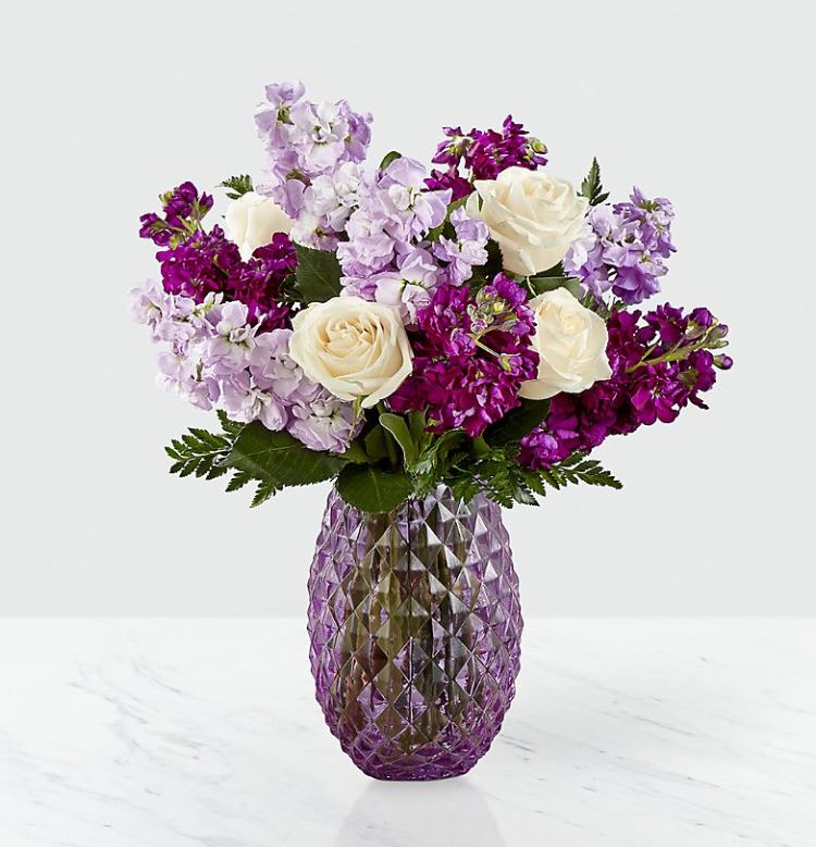 Sweet Devotion™ Bouquet  - et those know you hold them dear in a truly beautiful way. An array of cream roses and hues of violet stock burst from a lavender glass vase with a diamond pattern and comes together to create an artful collection of flowers. Whether it's a long-distance friend or a family member down the street, this collection of flowers makes for a sweet gift.