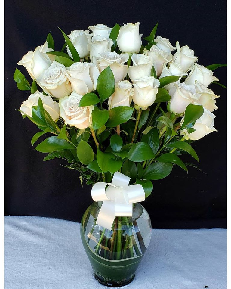 White roses arranged in a glass vase with a white ribbon