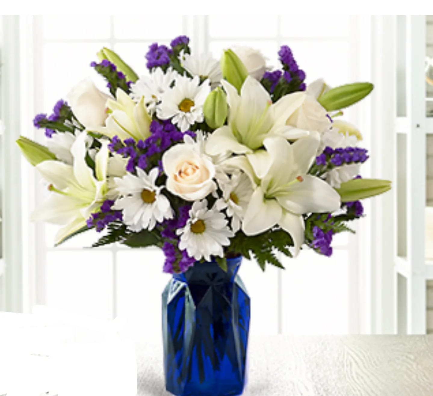 Beyond Blue™ Bouquet - VASE INCLUDED - Our Beyond Blue Bouquet features lilies, roses, carnations and lush greens to captivate your recipient. A collection of brilliant white blooms is contrasted by a stunning and bold blue vase. This arrangement makes an excellent thank you, get well or engagement gift! For sharing your sympathies, this bouquet is best fit to send to a home or residence.  