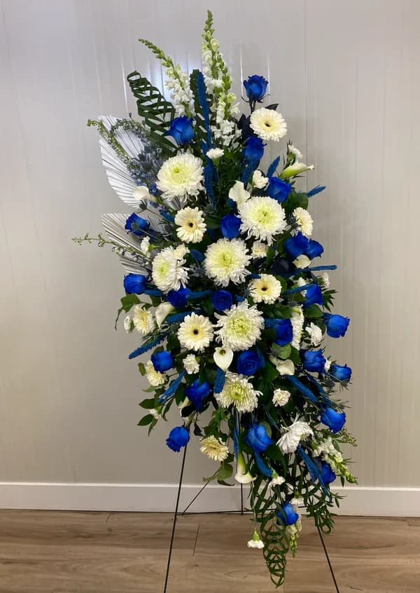Blue serenity (luxury line) - standing spray brings together an exquisite blend of vibrant blue roses, delicate white chrysanthemums, elegant calla lilies, elegant snapdragons, sunny gerbera daisies, and lush carnations, all artfully arranged against large palm leaves, to create an exquisite expression of love and sympathy.  (Not available for same day orders)