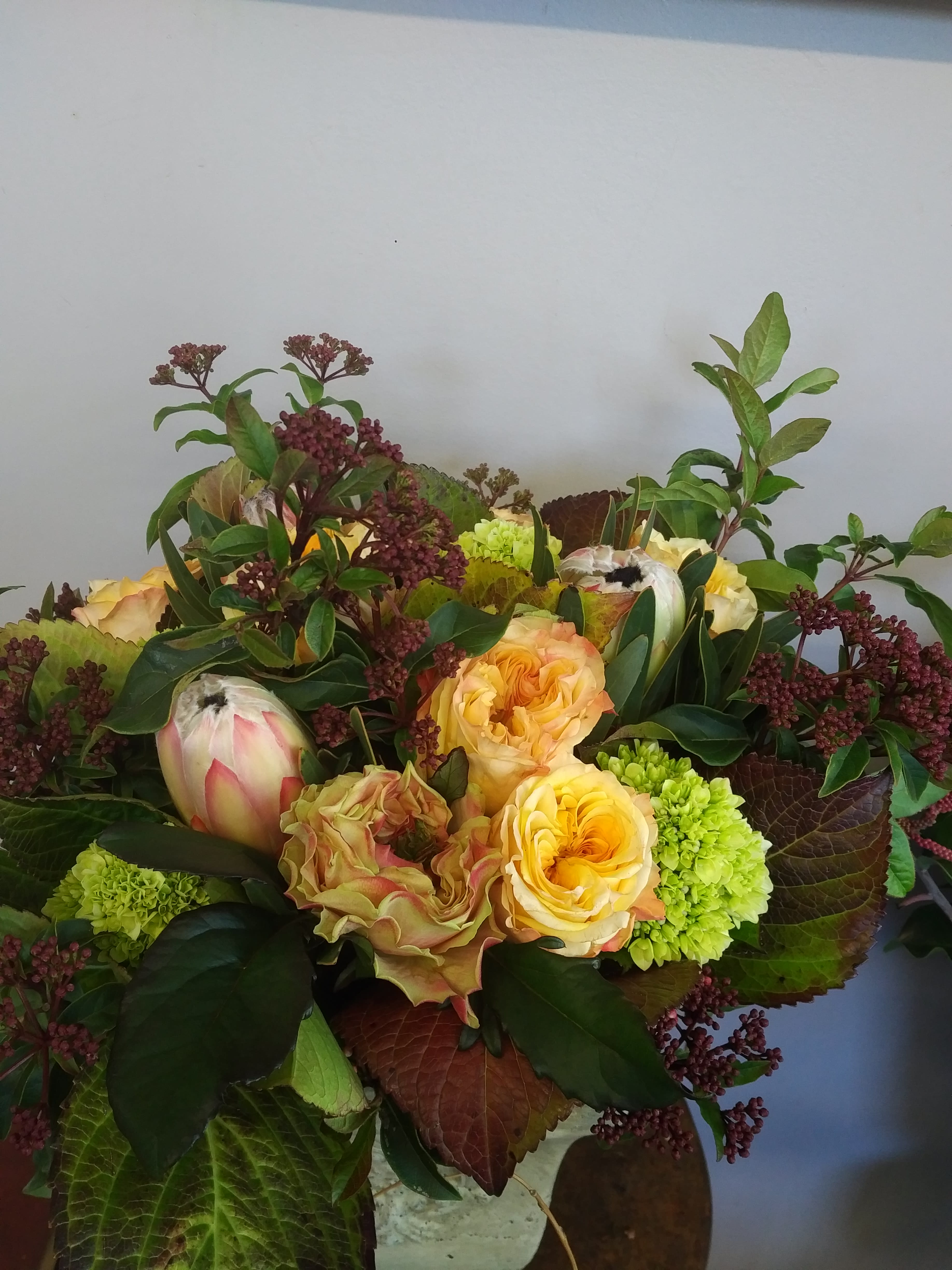 Bouquet of yellow roses and green blooms with burgundy foliage
